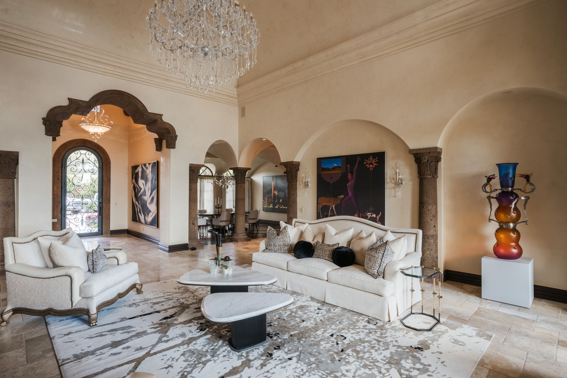 Luxurious living room: cream walls, marble floor, white sofa, abstract rug, artwork, ornate ceiling, chandelier.