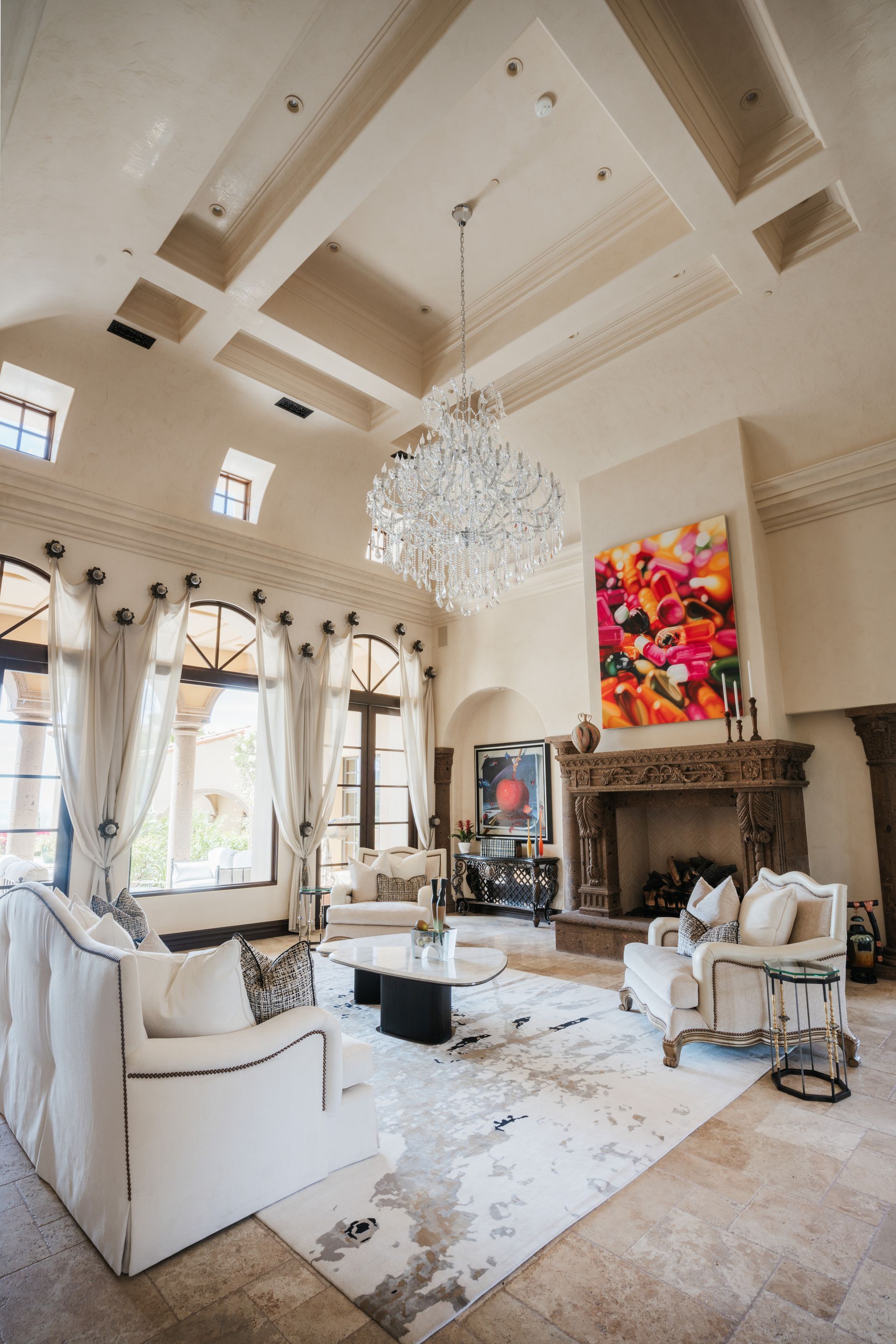 Luxurious living room with white furniture, large chandelier, fireplace, and abstract art.