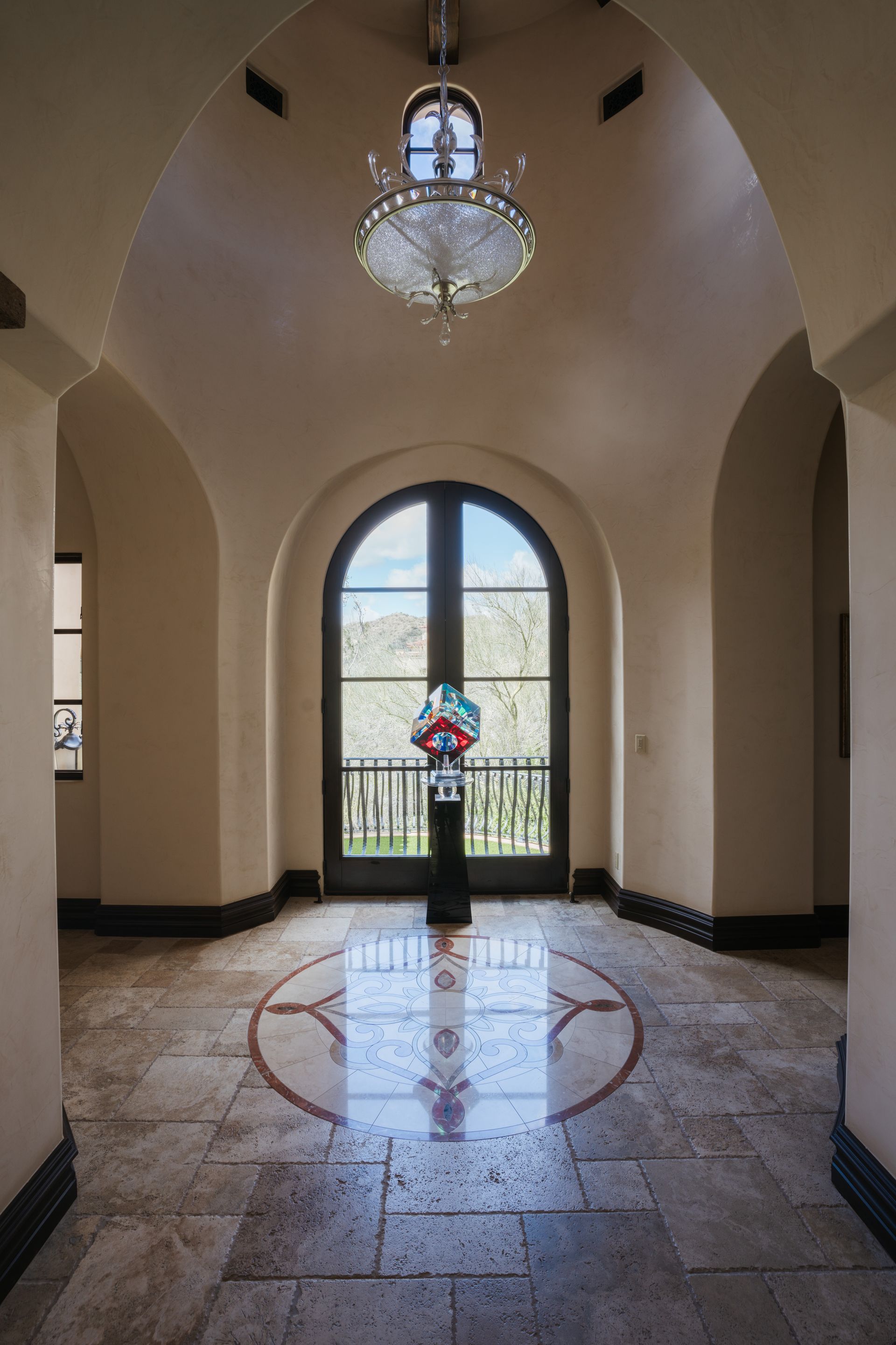 Ornate entryway with arched doorway, chandelier, patterned floor, and sculpture.