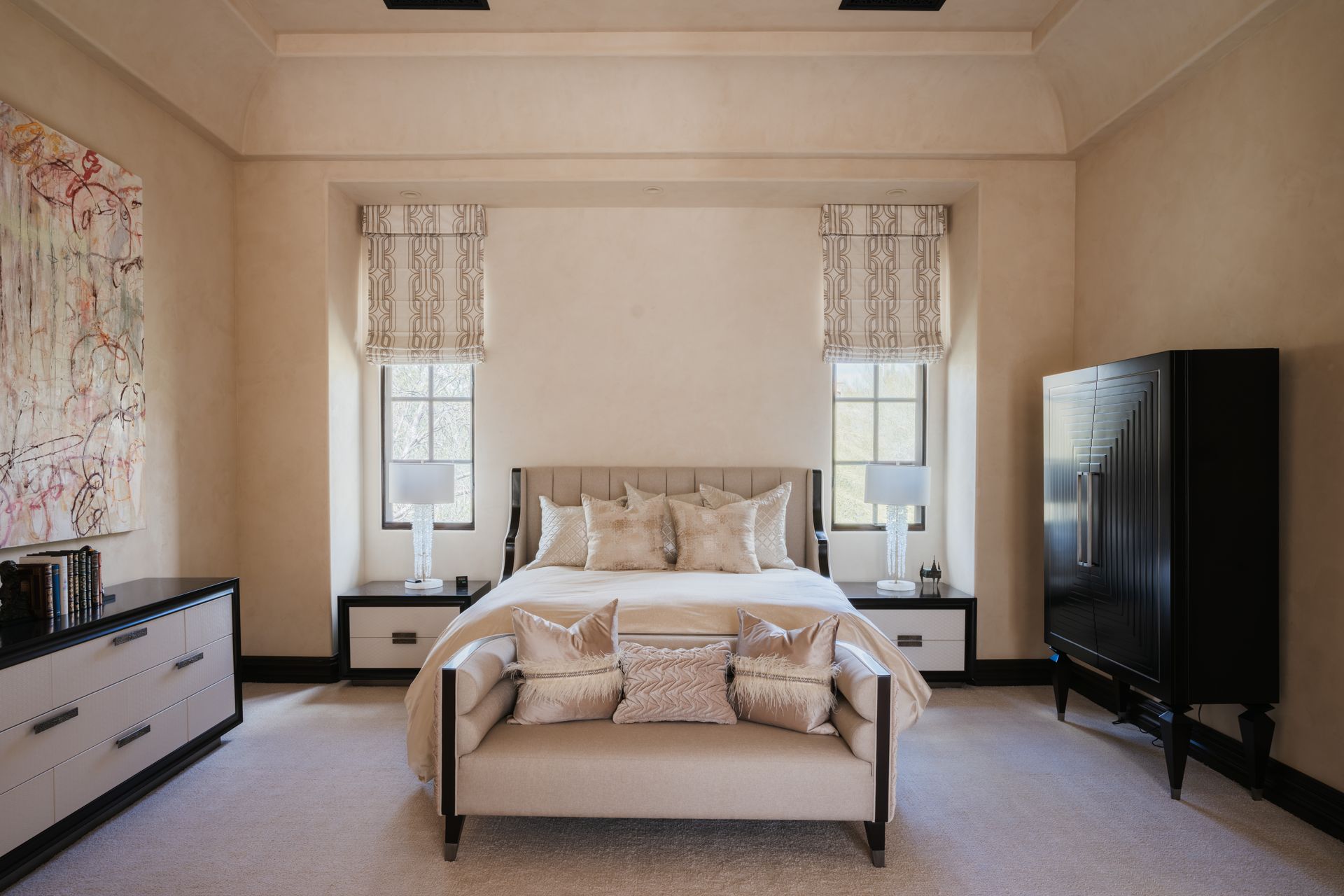 A beige bedroom with a bed, bench, two windows, two bedside tables, a dresser, and a wardrobe.