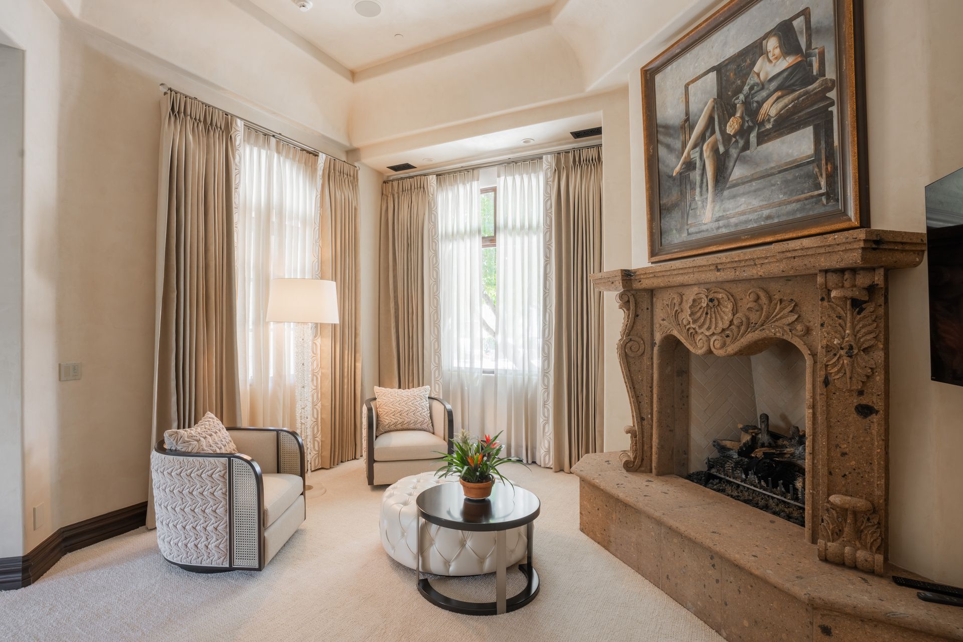 Elegant living room with fireplace, chairs, and large window with draped curtains.