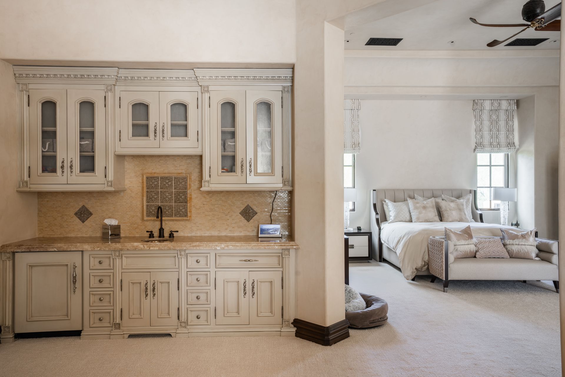 Wet bar with distressed white cabinets, tan counter, and bedroom in the background.