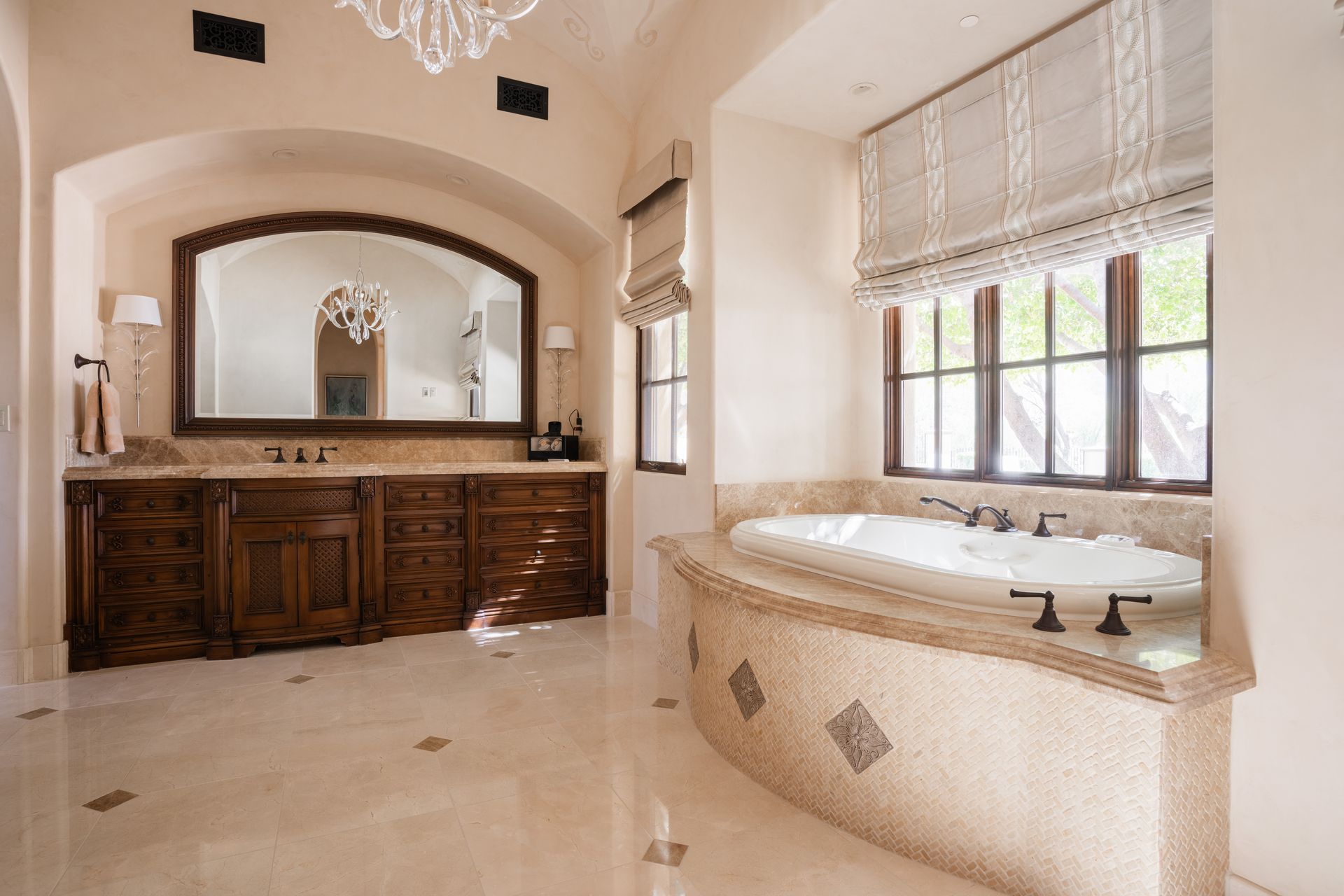 Luxurious bathroom with a mosaic-tiled tub, wooden vanity, and large arched mirror.