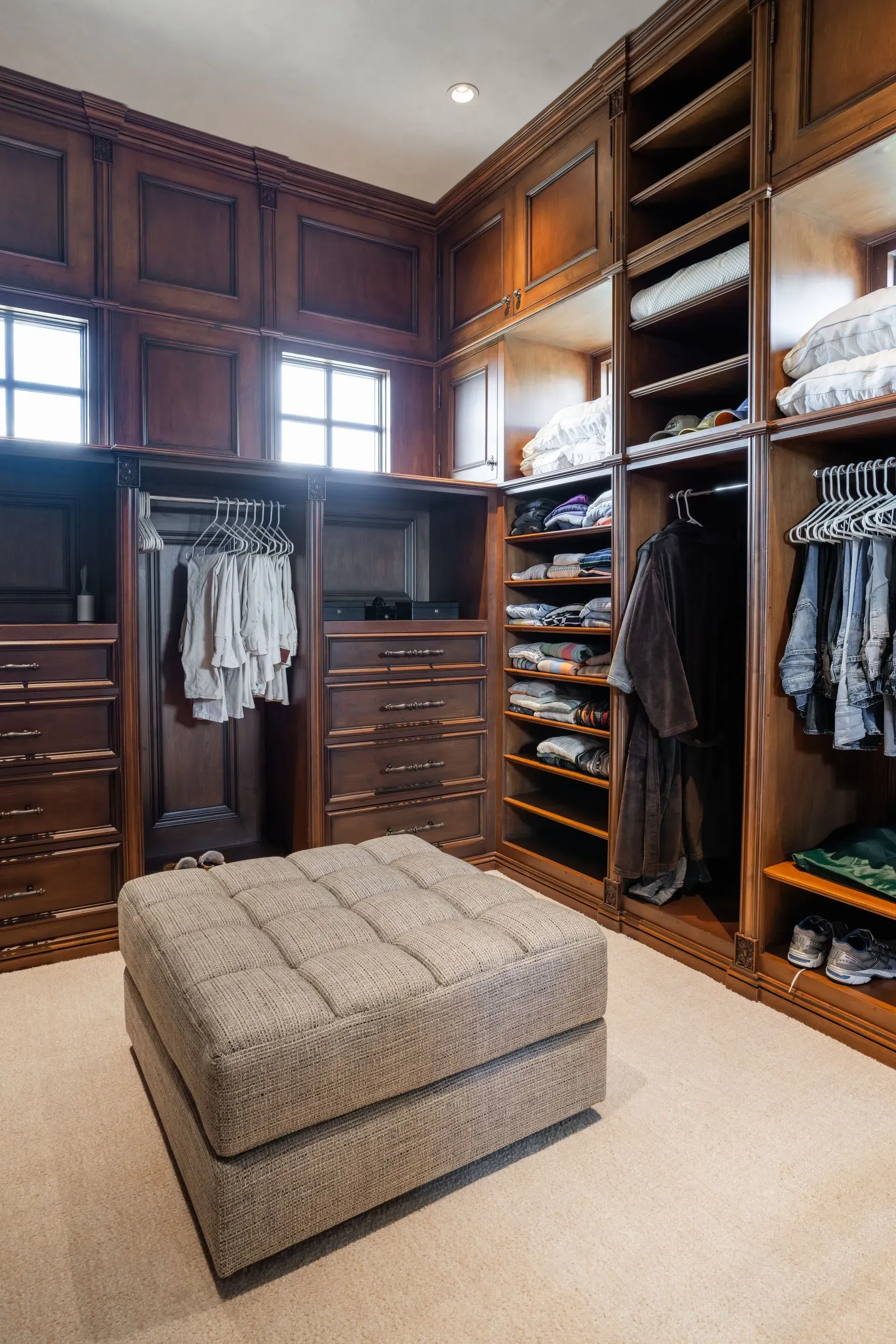 Walk-in closet with dark wood cabinetry, shelves of folded clothes, hanging garments, and an ottoman.