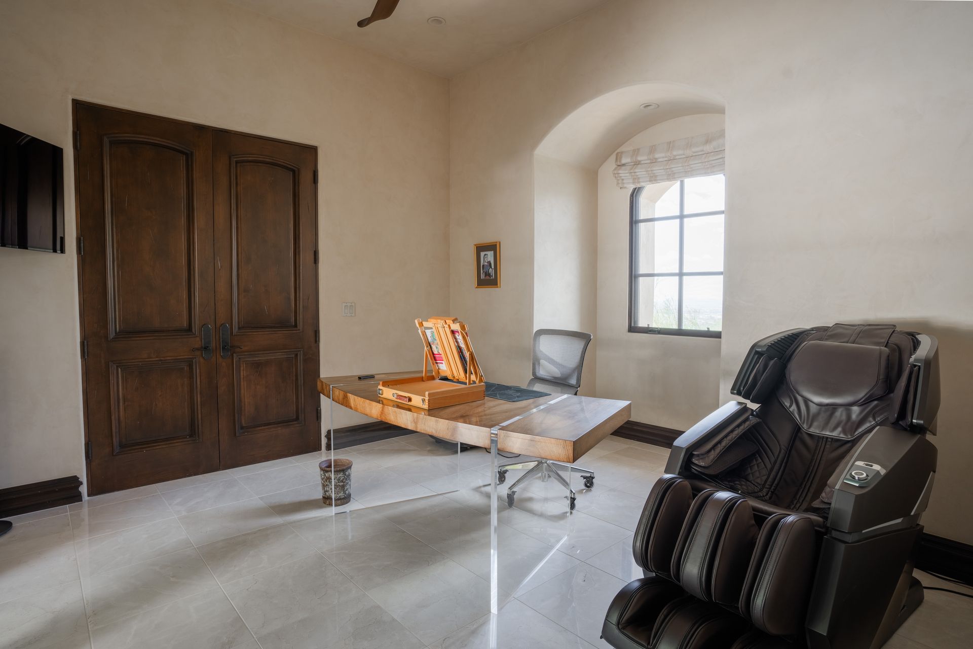 Office with wooden double doors, desk, massage chair, window, and glossy floor.