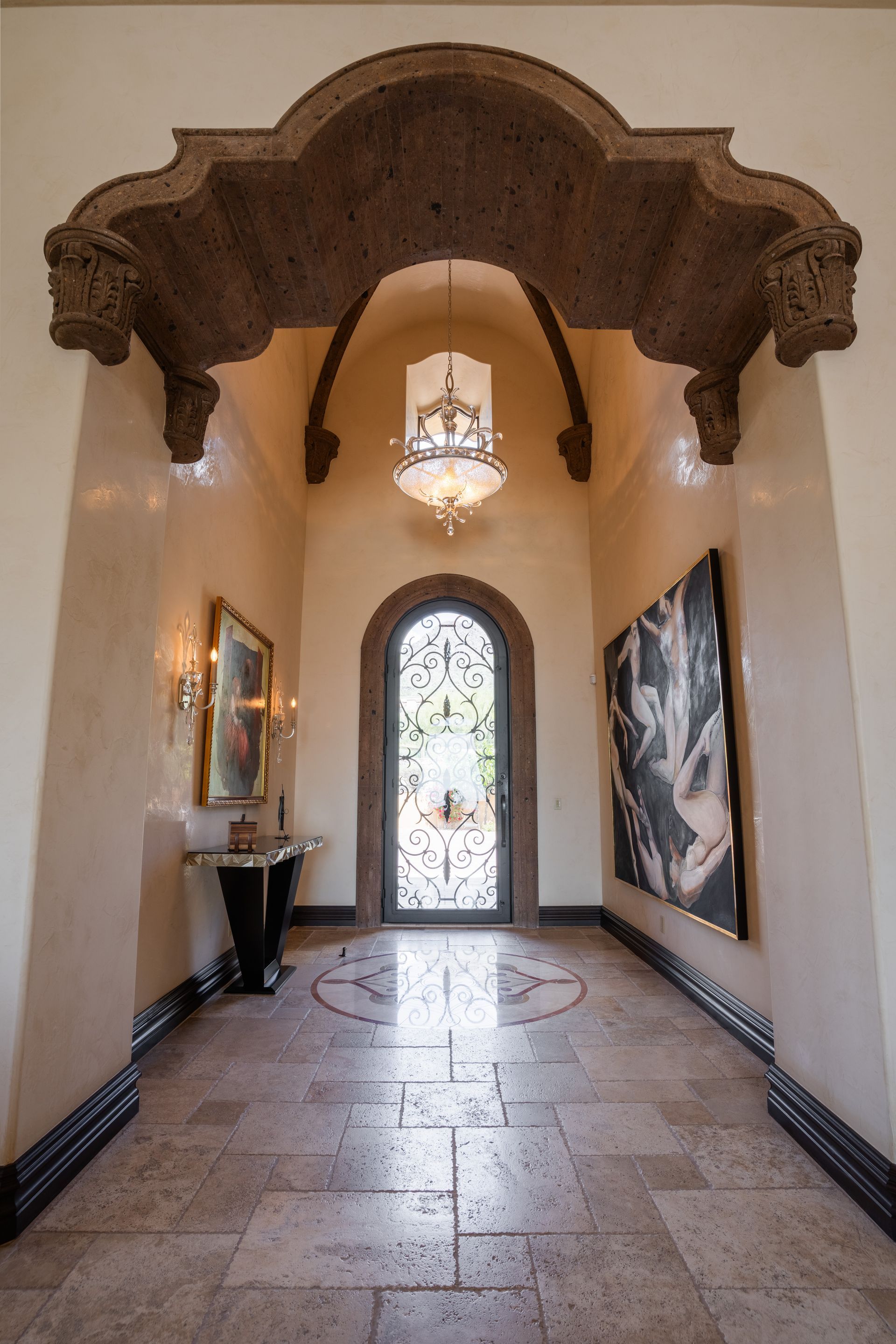 Hallway with ornate archway, tile floor, artwork, and chandelier.