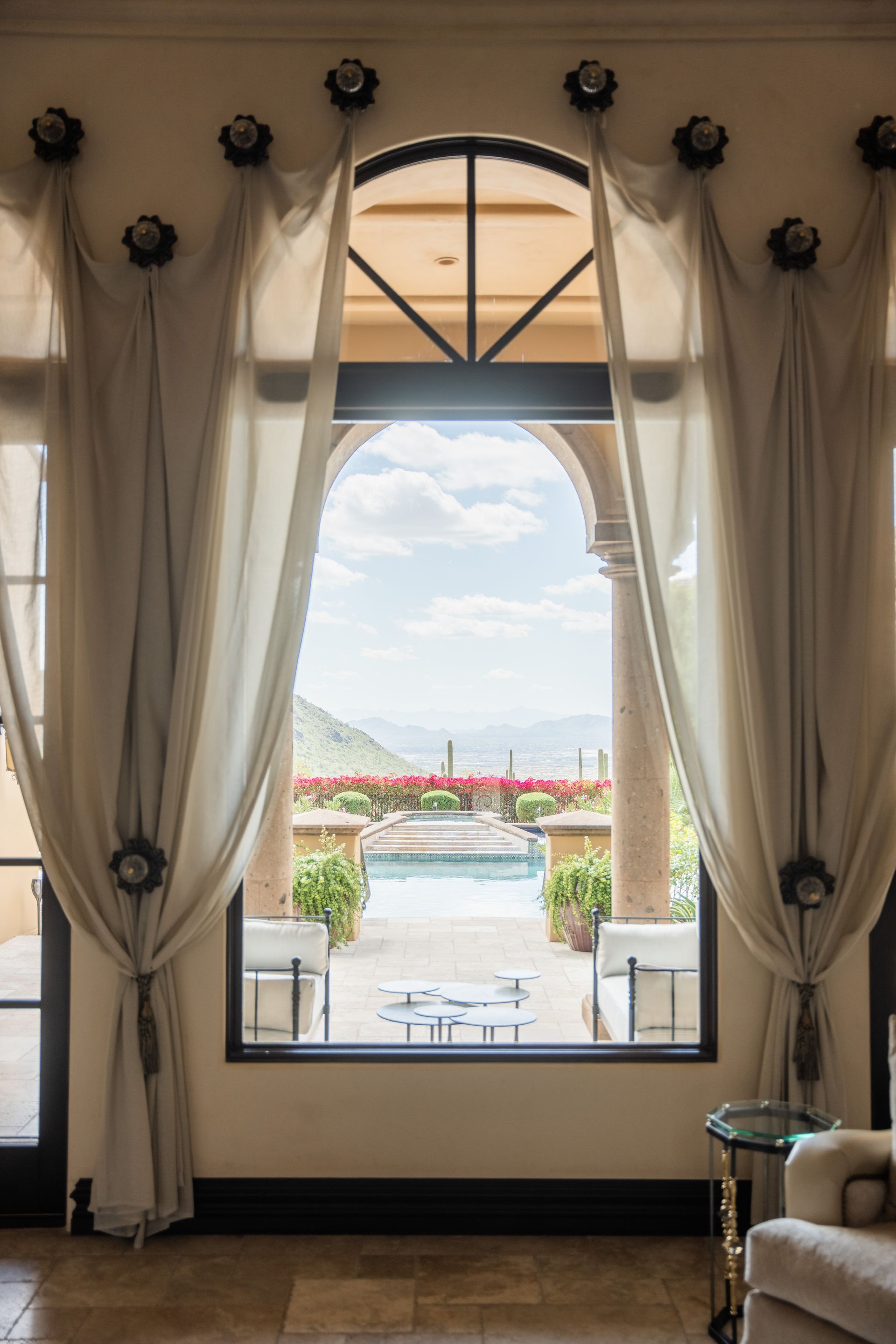 Elegant window with sheer curtains frames an outdoor pool and mountain view.