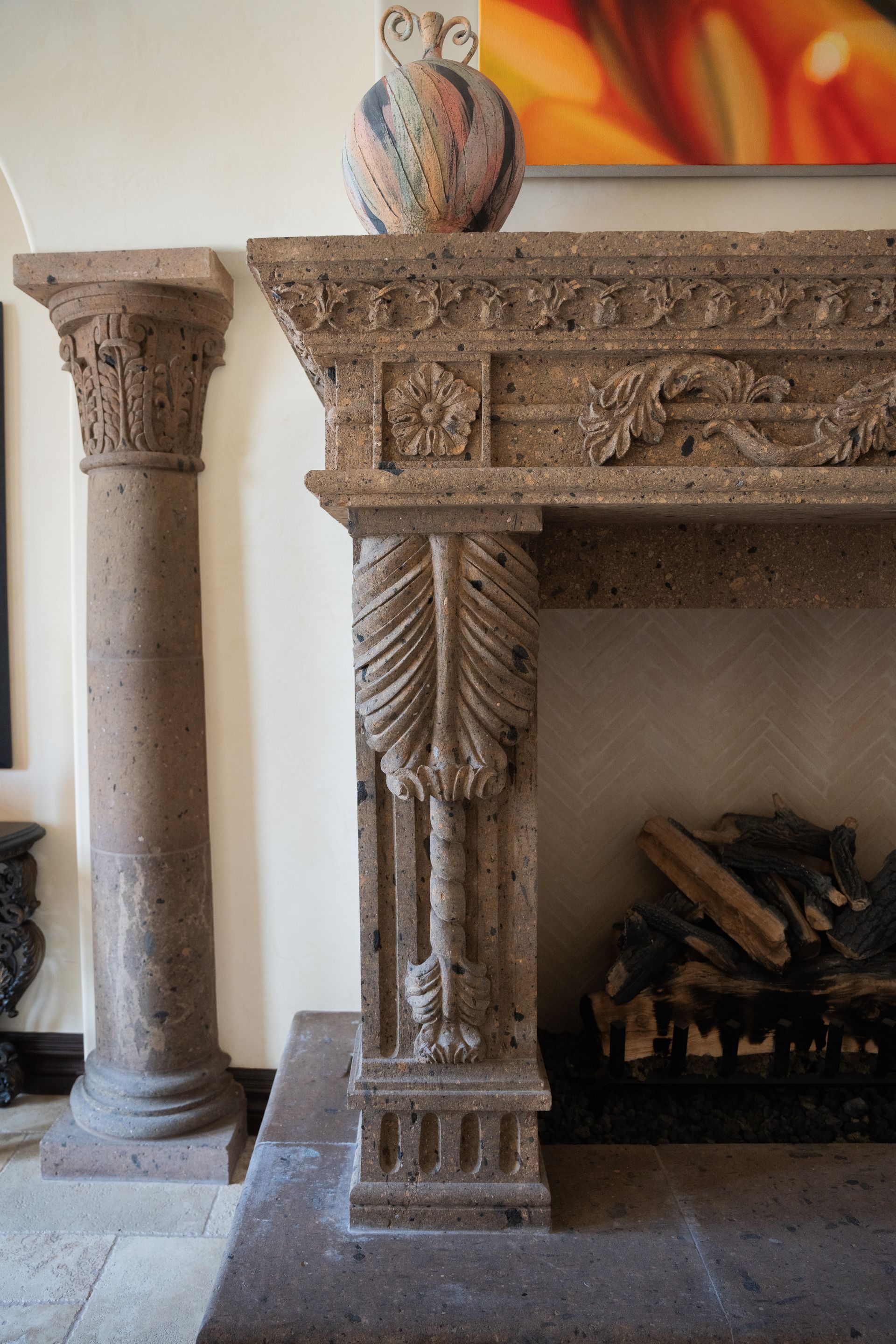 Stone fireplace with carved details, next to a column; vase on the mantel.