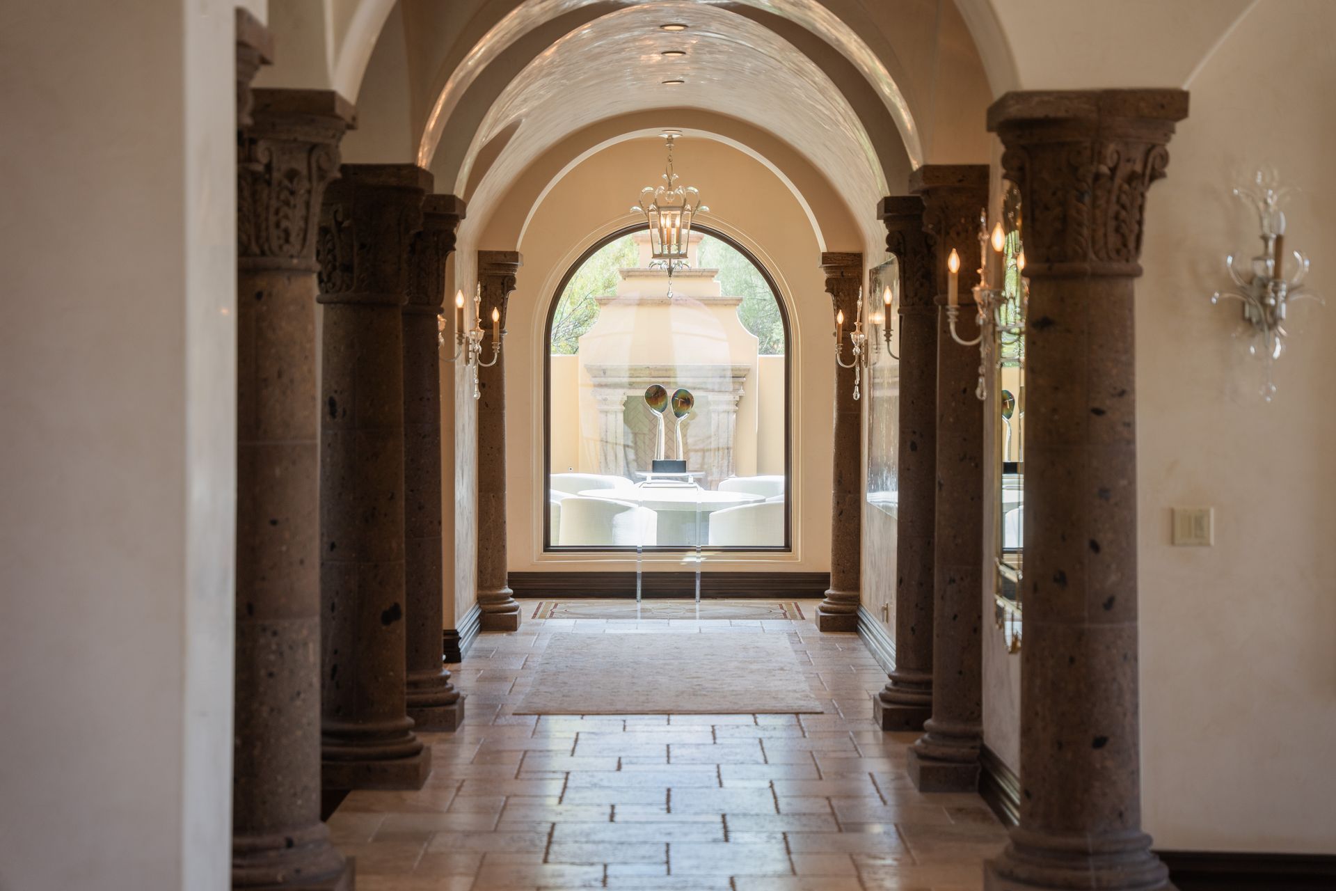 Stone colonnade leads to arched window overlooking fountain.
