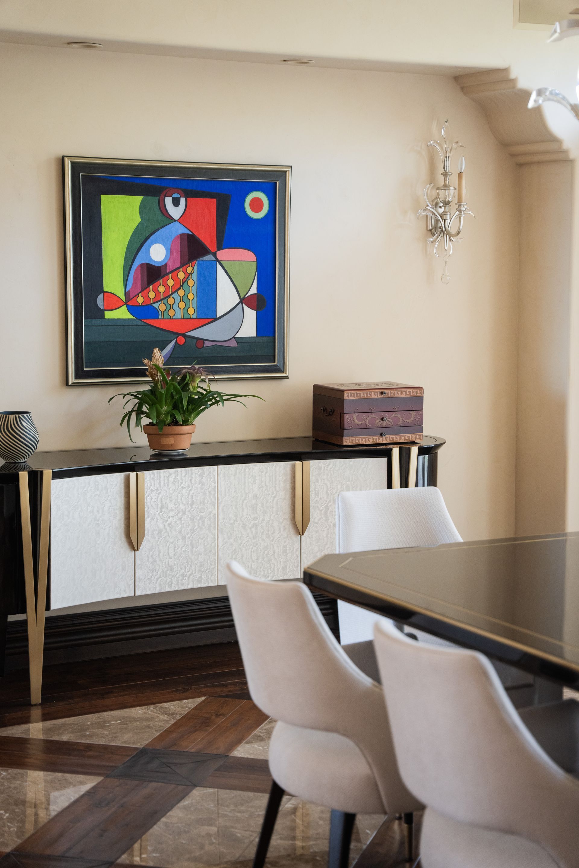 Dining room with abstract art, sideboard, chairs, and table. Beige walls and elegant lighting fixtures.