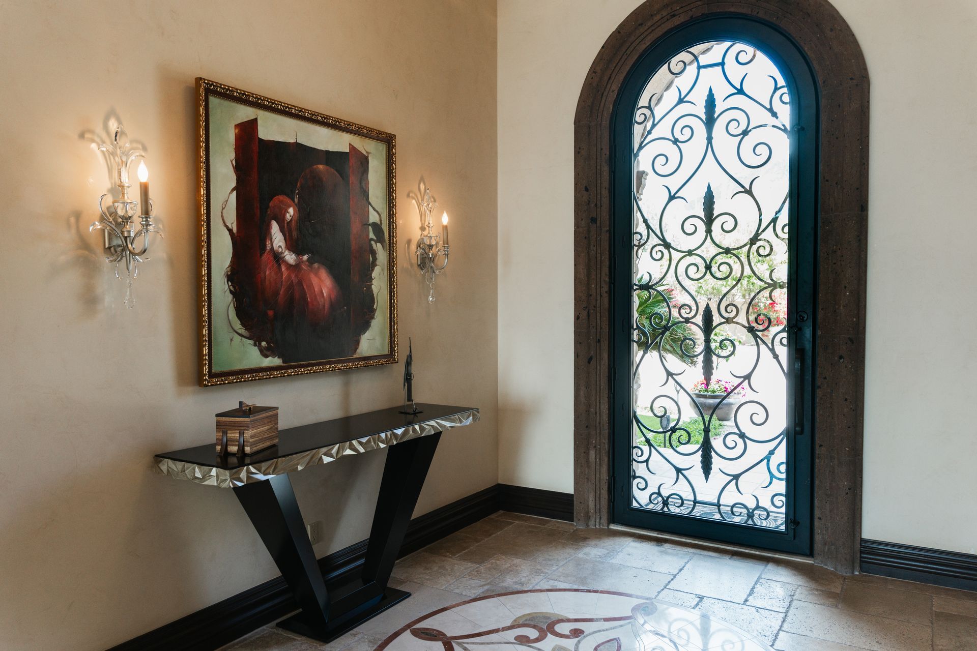 Elegant entryway with artwork, console table, and ornate wrought-iron door.
