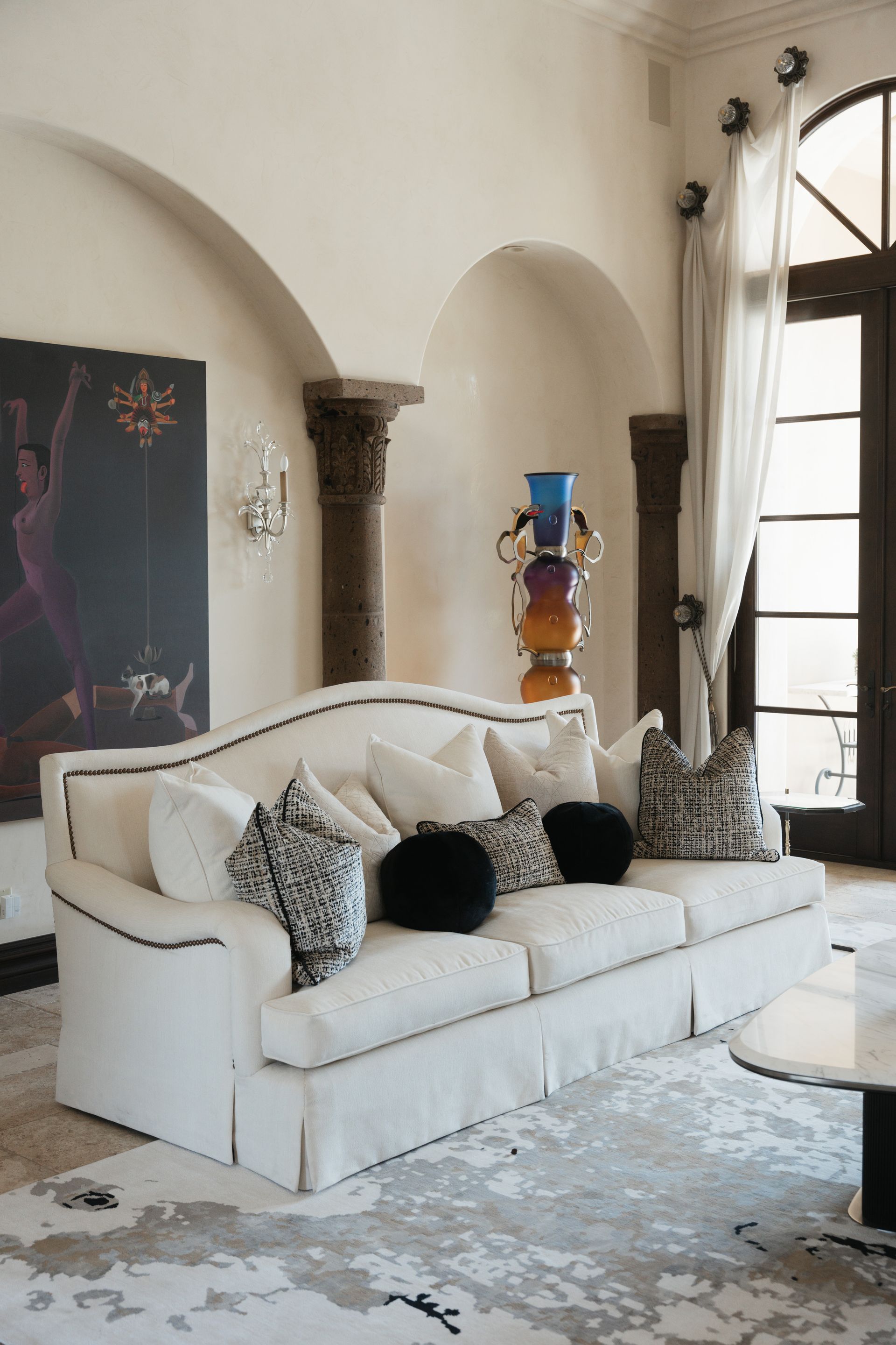 Living room with white sofa, decorative pillows, artwork, and arched doorways.