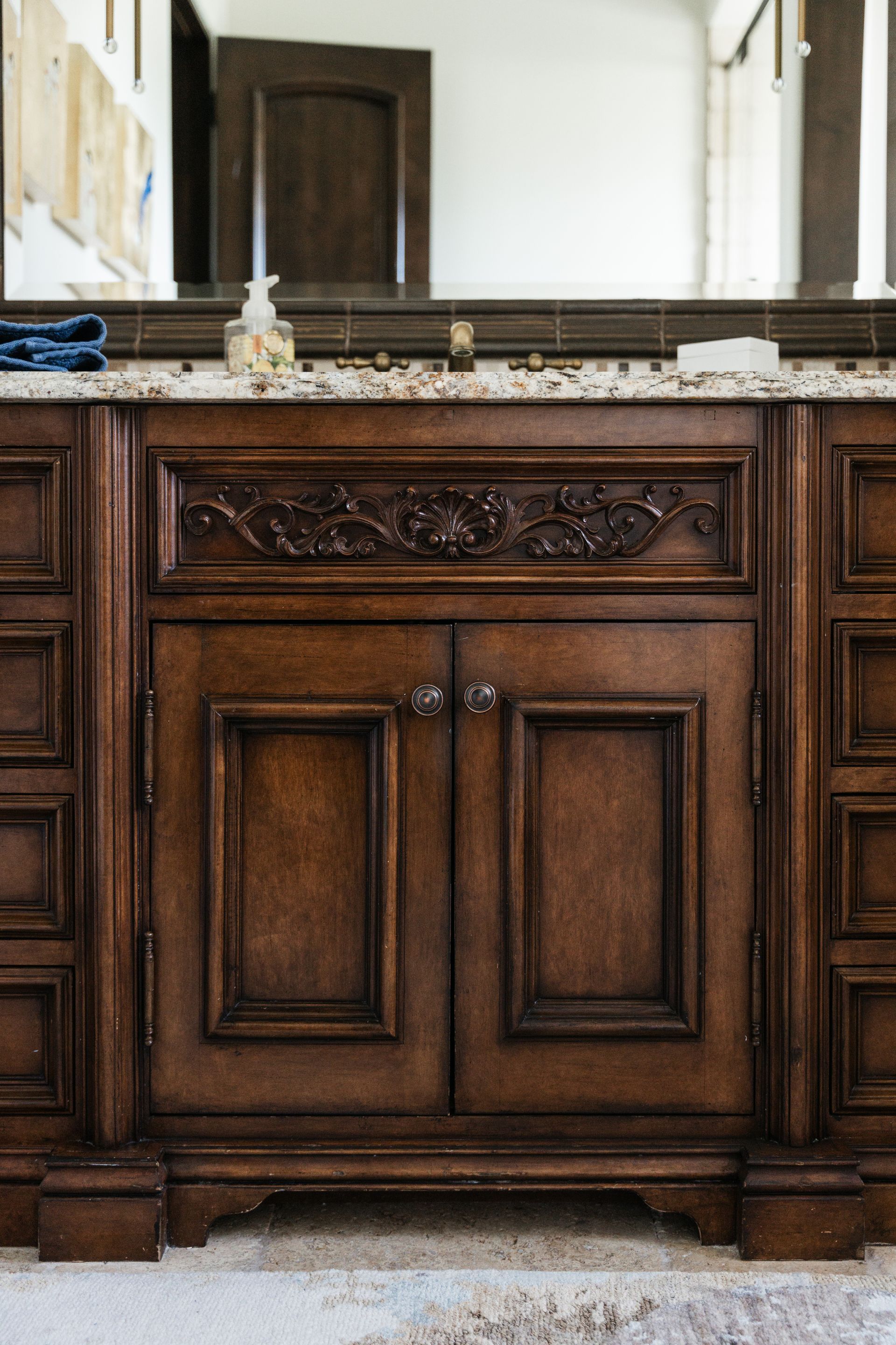 Wooden bathroom vanity with carved details, granite countertop, and mirror.