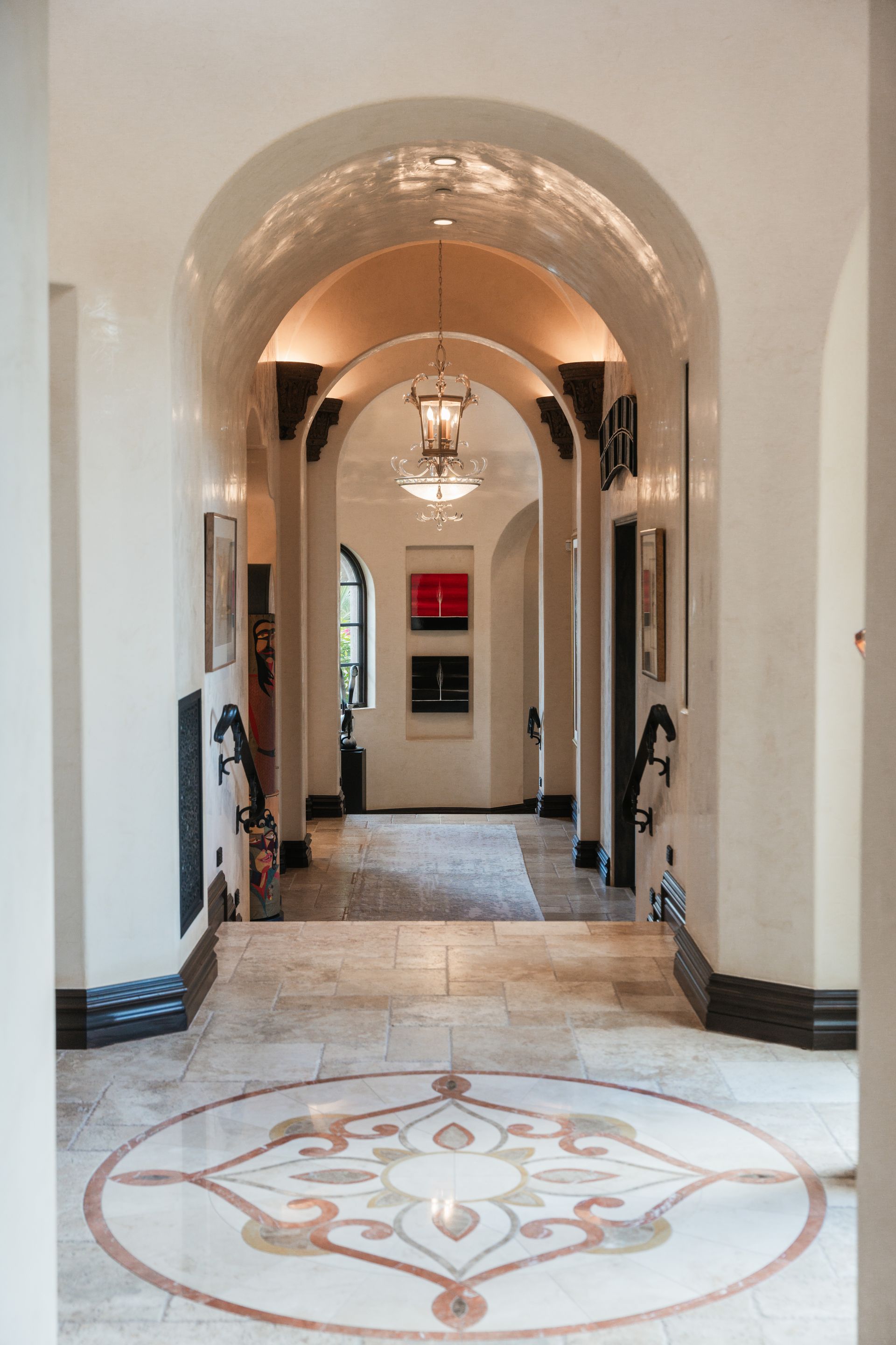 Elegant hallway with arched ceiling, mosaic floor design, and hanging lights.