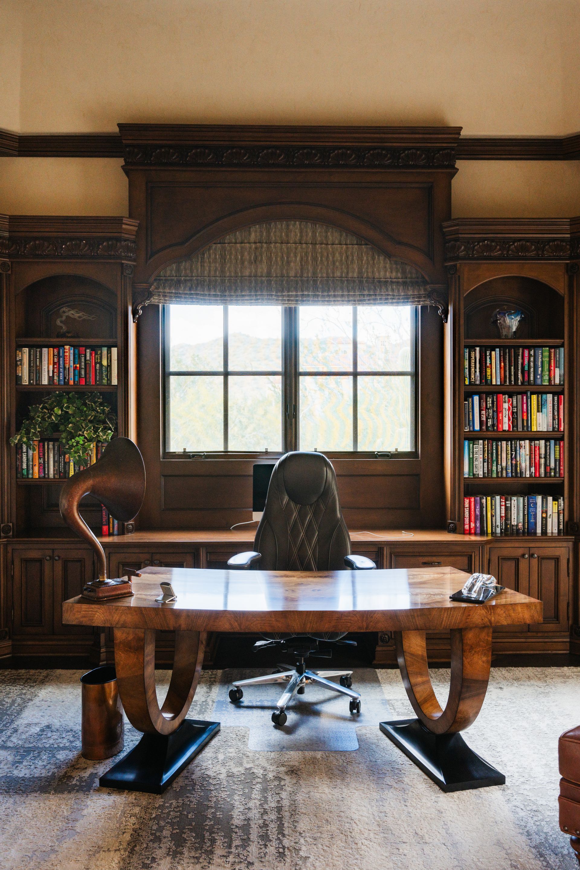 Elegant home office with dark wood desk, bookshelves, and arched window.