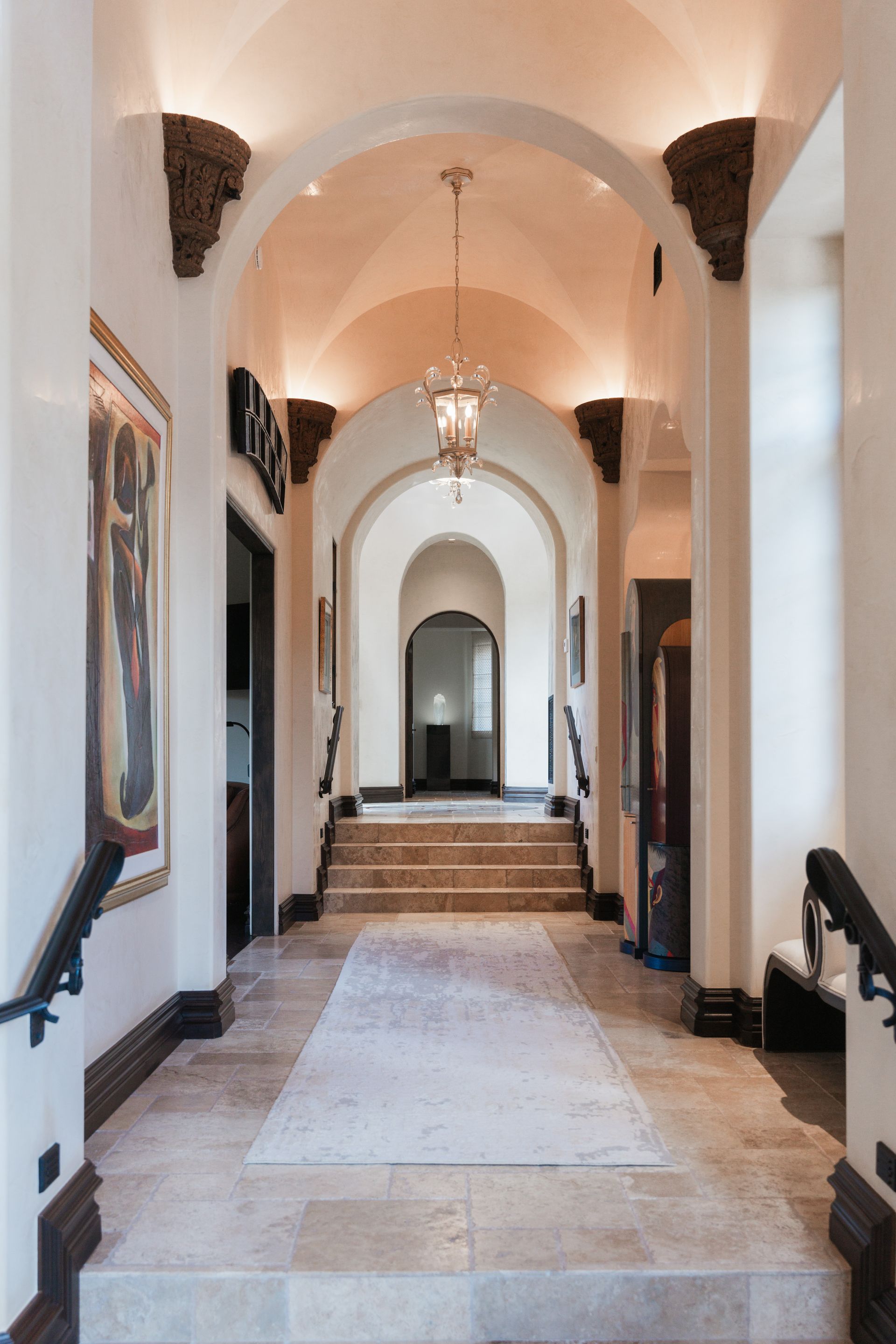 Hallway with arched doorways, ornate ceiling, and stone flooring.