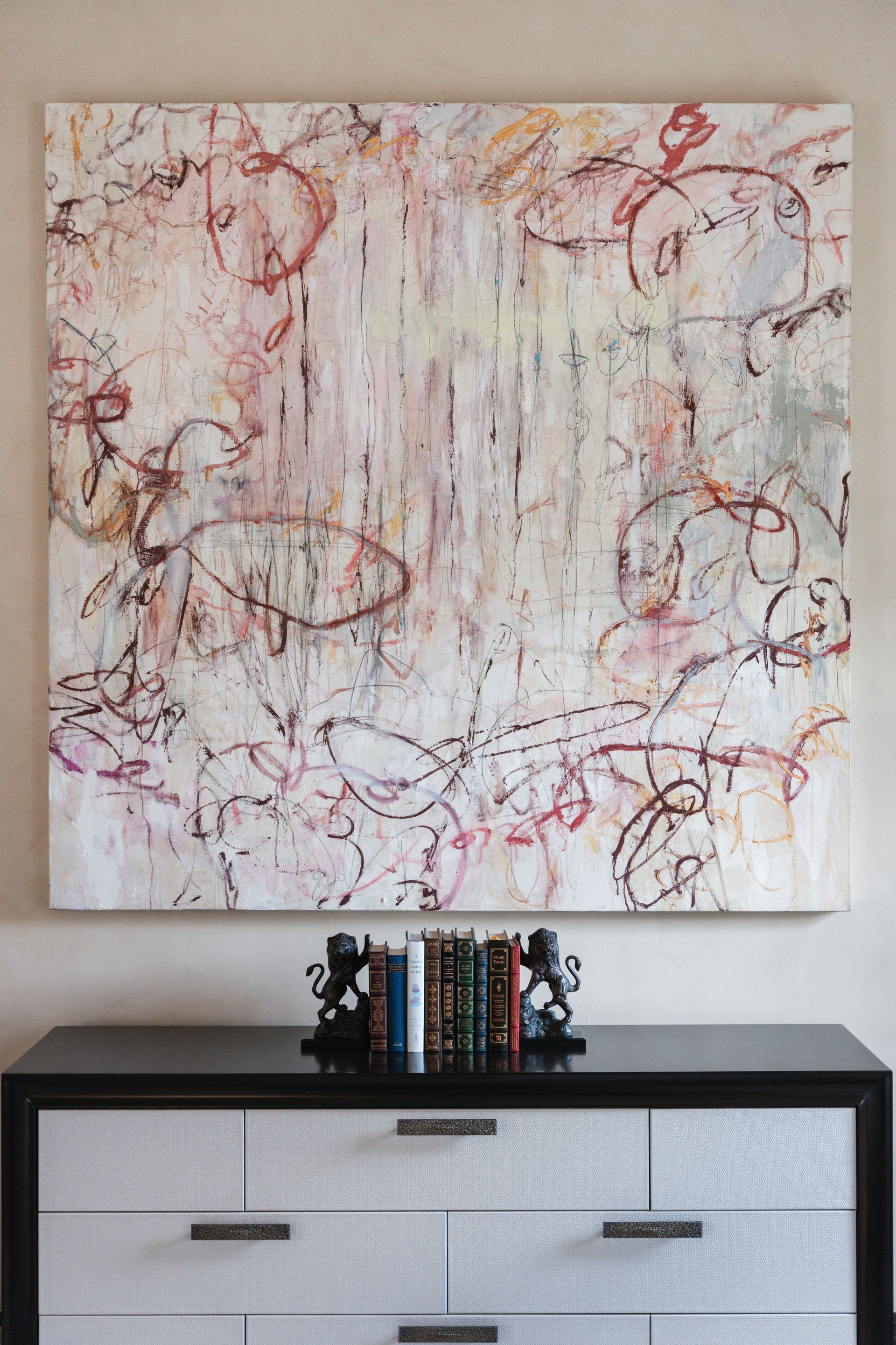 Abstract painting on wall above a dresser with books and bookends.