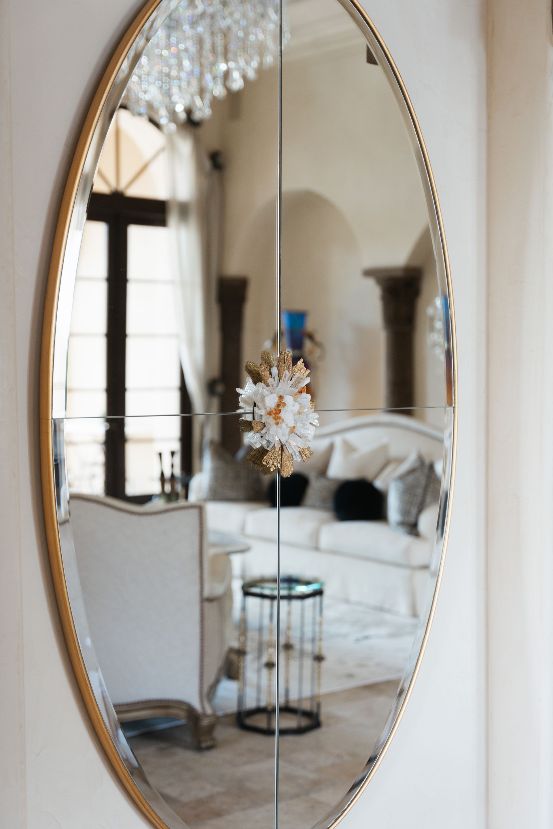 Oval mirror reflecting a living room with white furniture, a side table, and pillars.