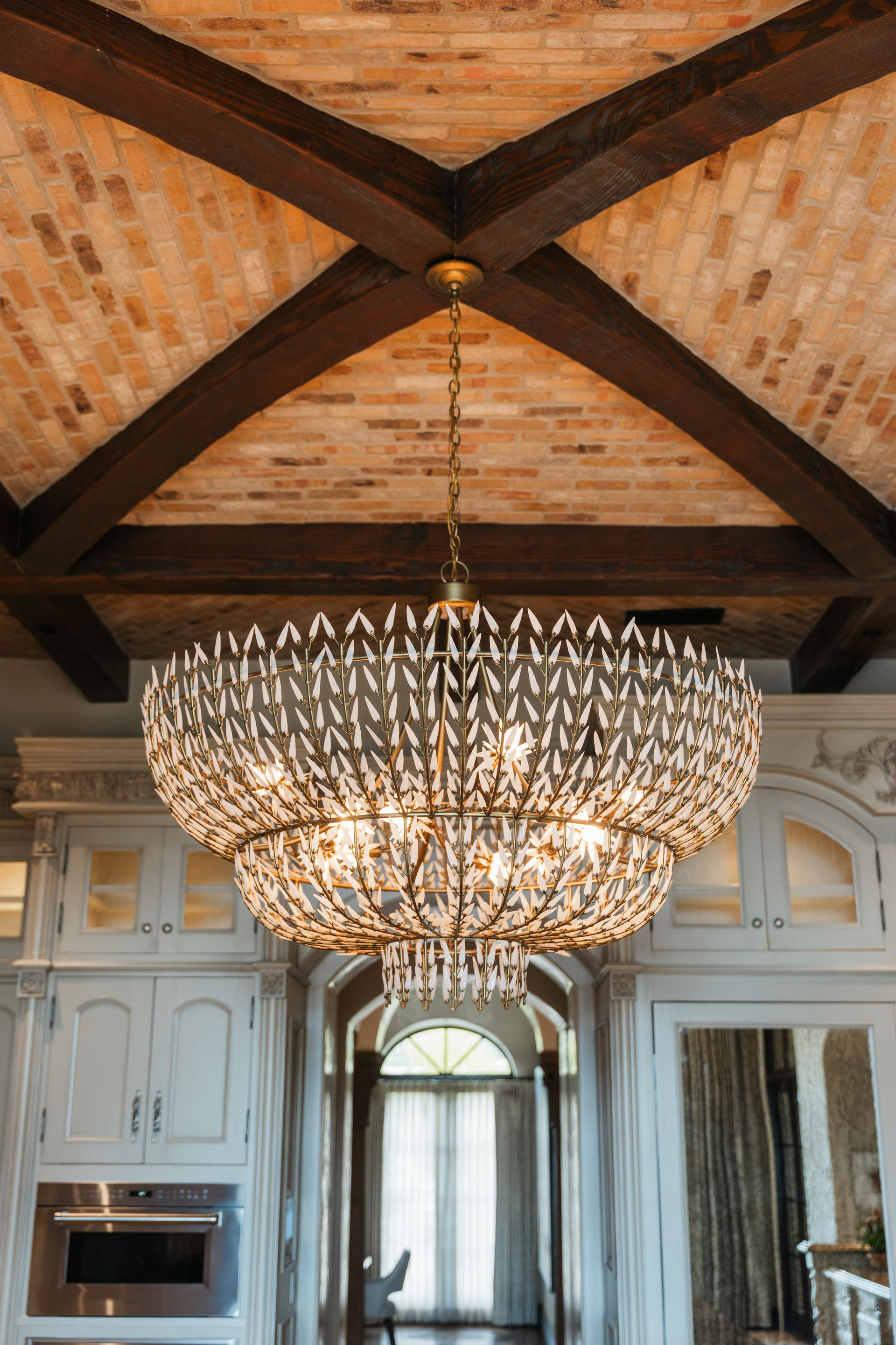 Large chandelier hanging in a room with a brick ceiling and wooden beams.
