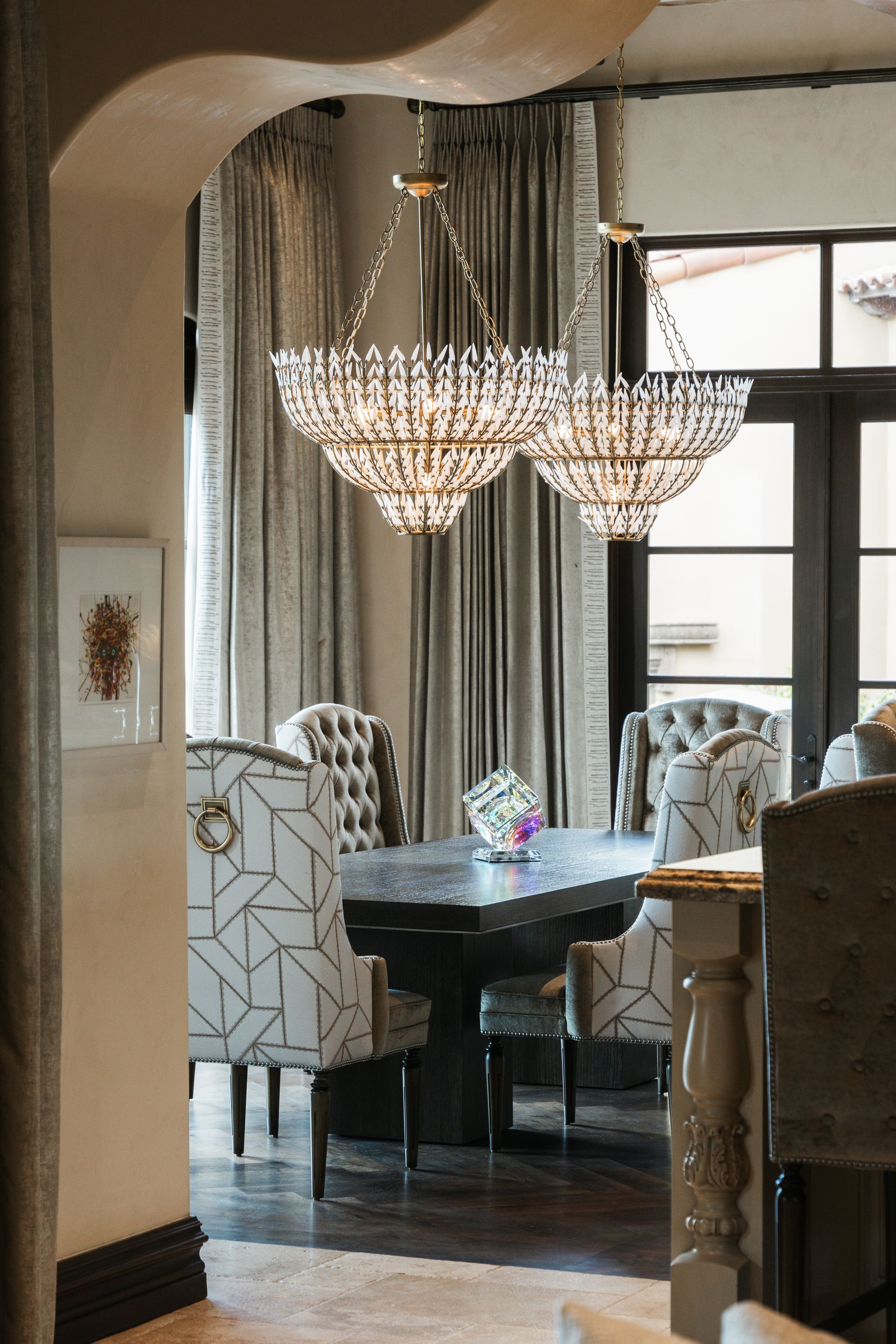 Dining room with dark table, patterned chairs, and crystal chandeliers.