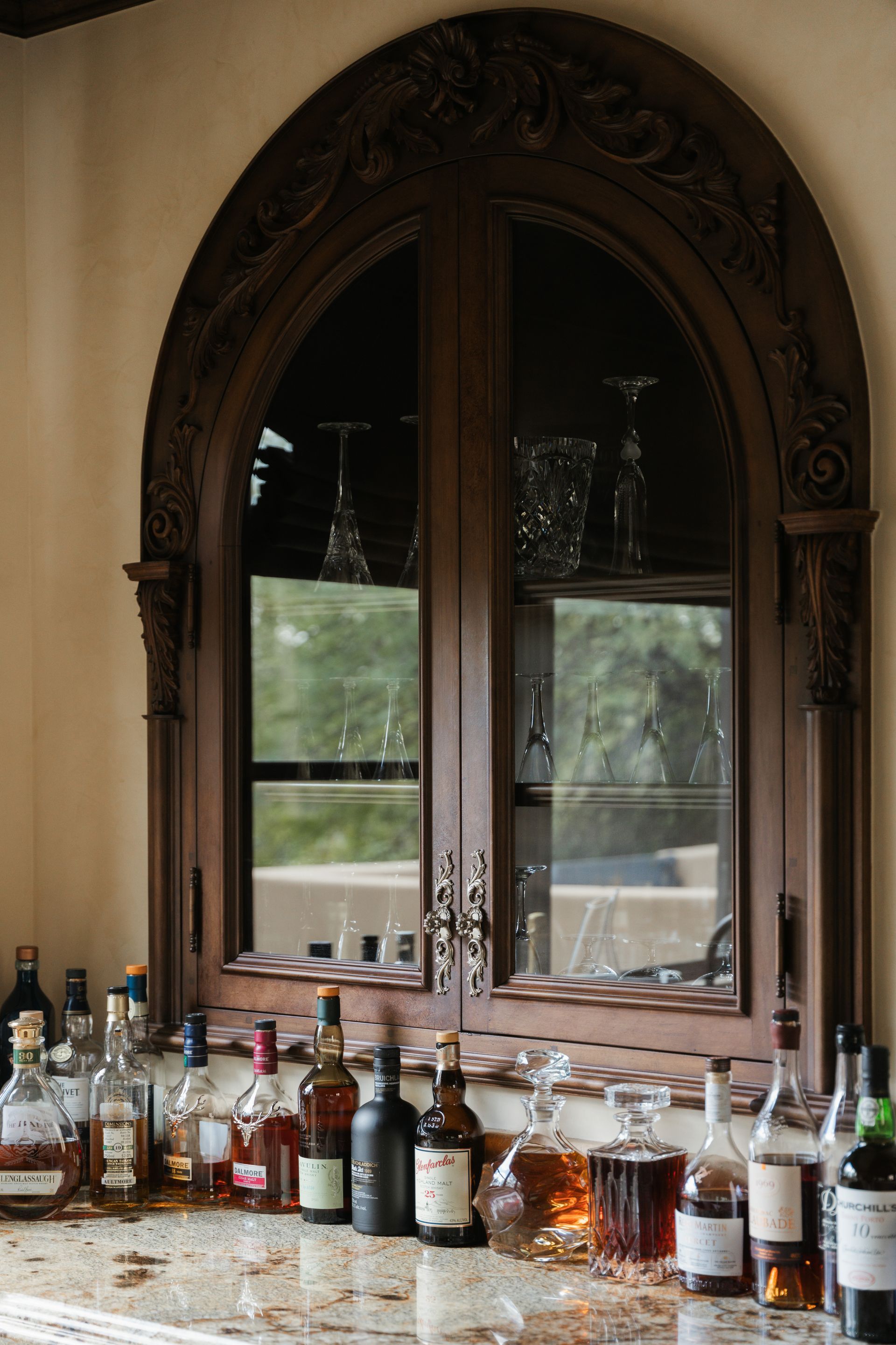 Dark wooden arched bar cabinet with bottles and glasses.