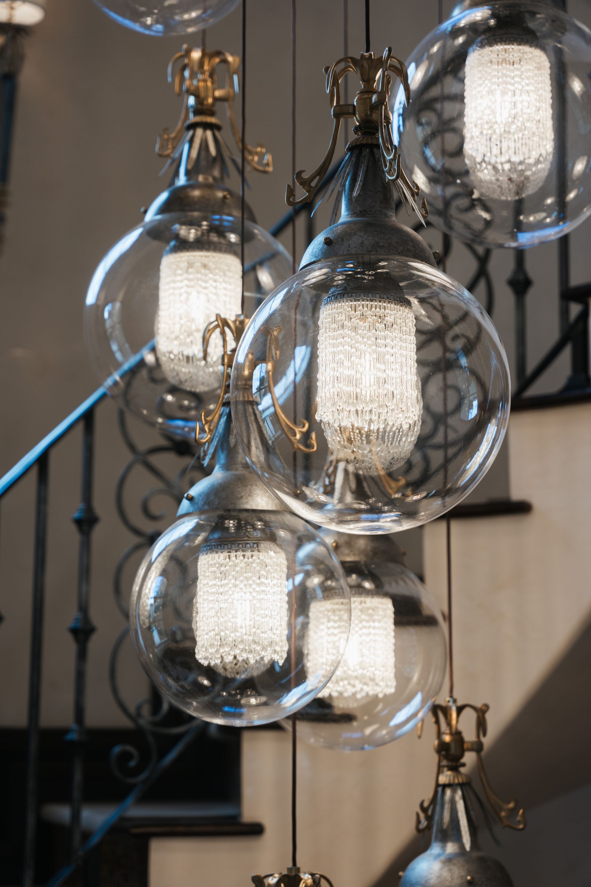 Elegant chandelier with glass globe shades, over stairs with dark railing.