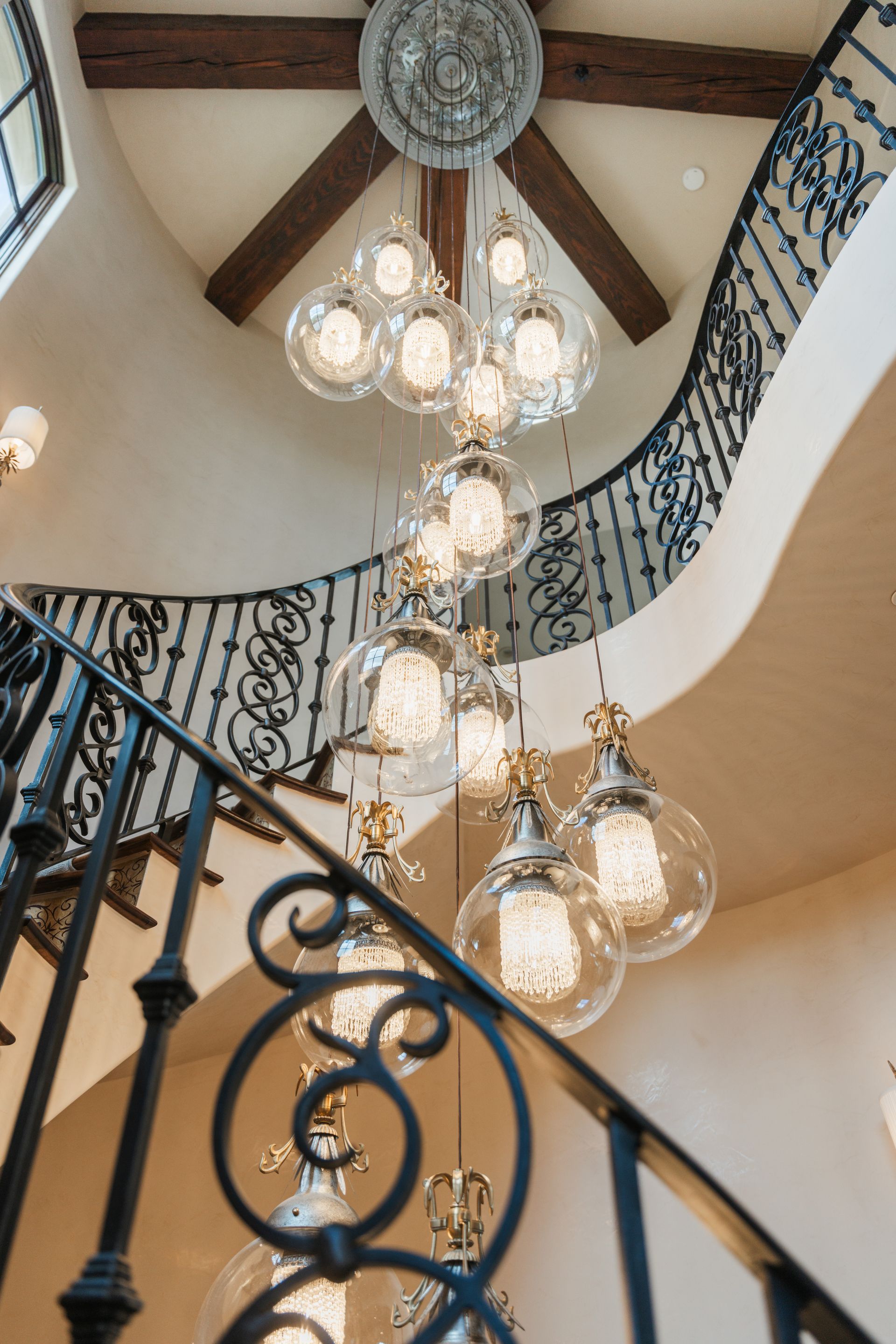 Ornate staircase with a winding wrought iron railing and a large chandelier with spherical lights.