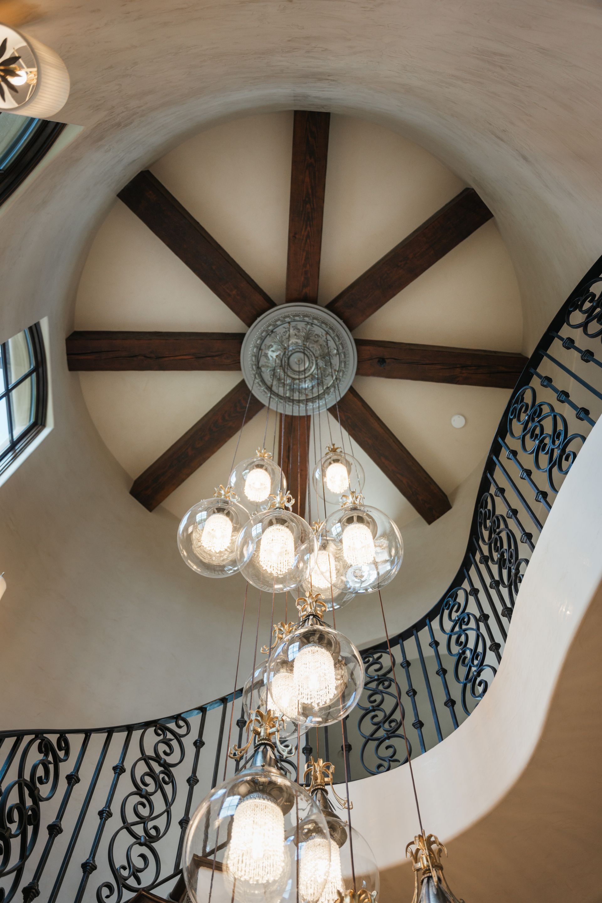 Ornate staircase with large globe pendant chandelier, circular ceiling with wooden beams.