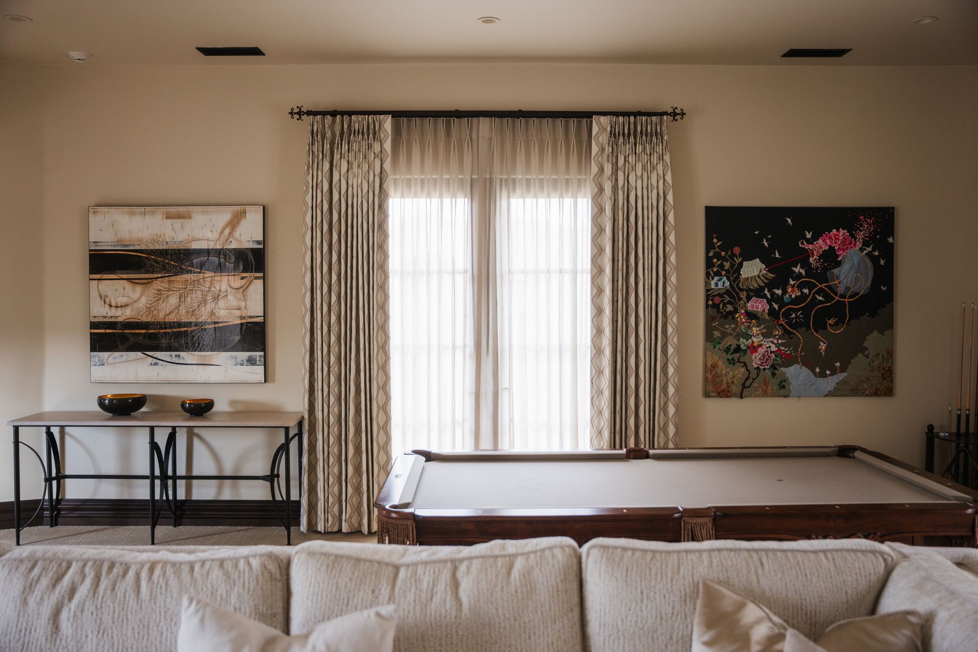 Pool table in a beige room with art, a console table, and patterned curtains.