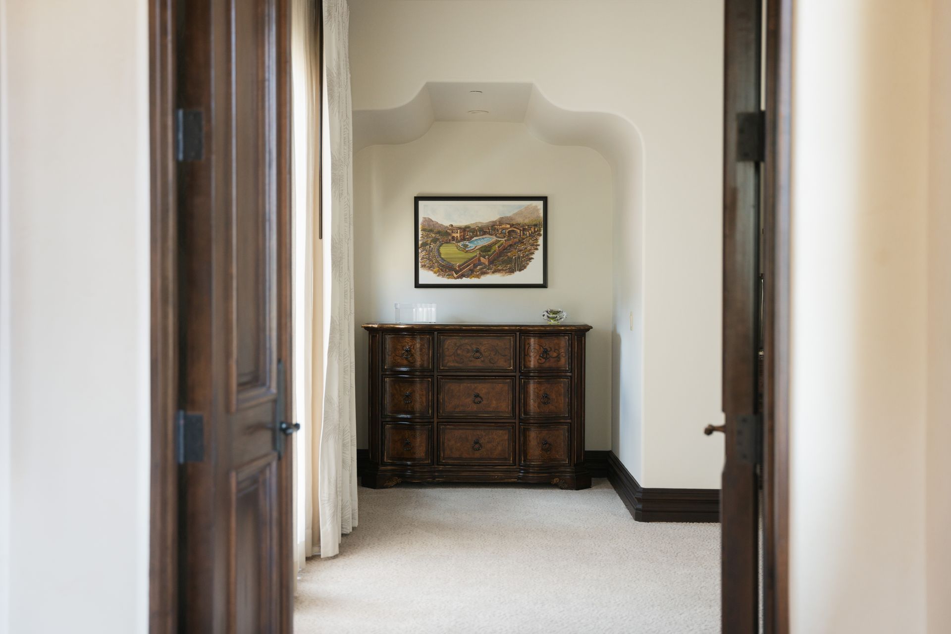 Open wooden doors frame a hallway with a cabinet and artwork in an alcove.
