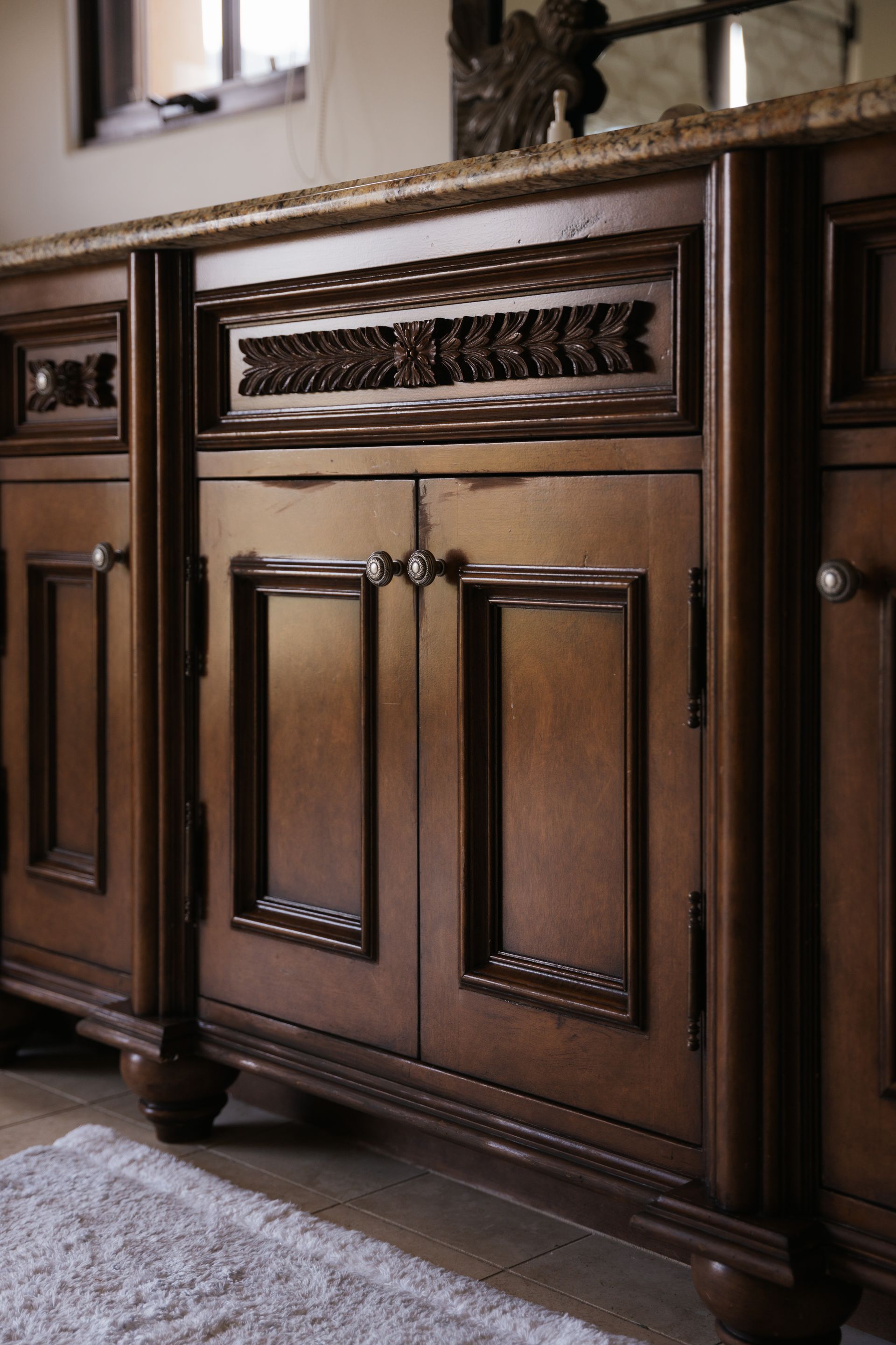 Dark brown bathroom vanity with granite countertop and ornate carvings.