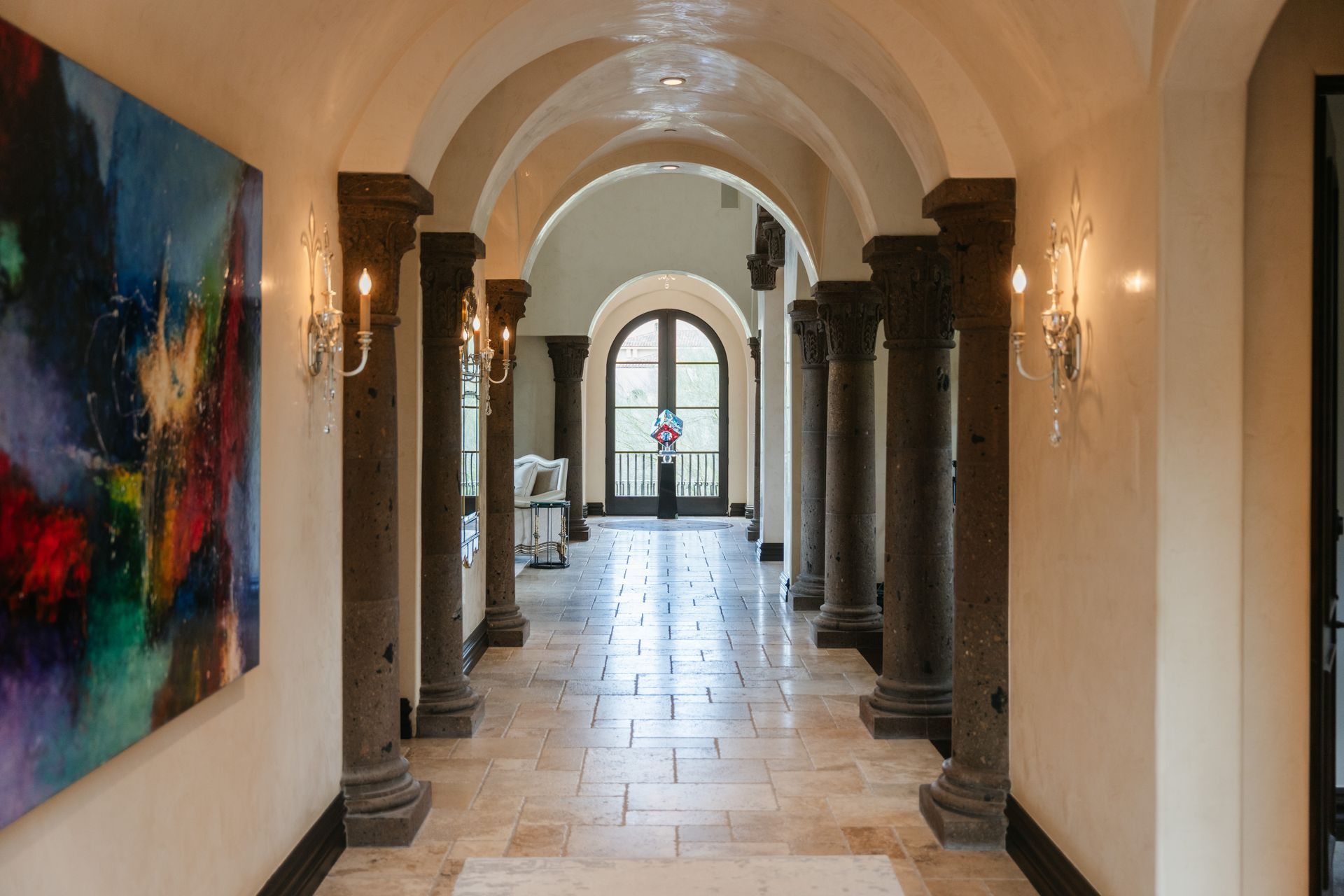 Hallway with arched columns and tile floor, abstract painting on left, and front door at end.