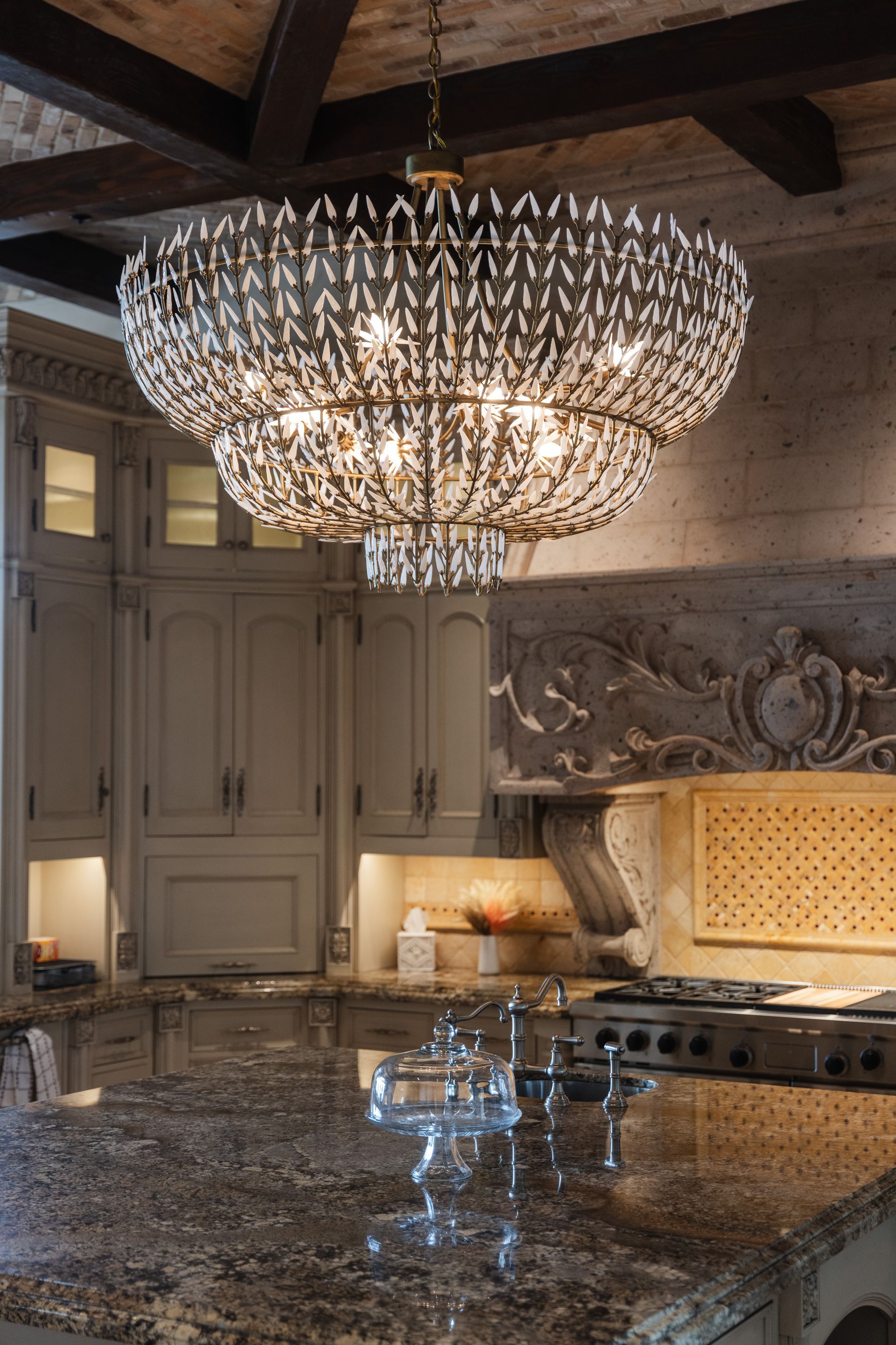 Kitchen with tiered crystal chandelier, granite countertops, and light-colored cabinets.