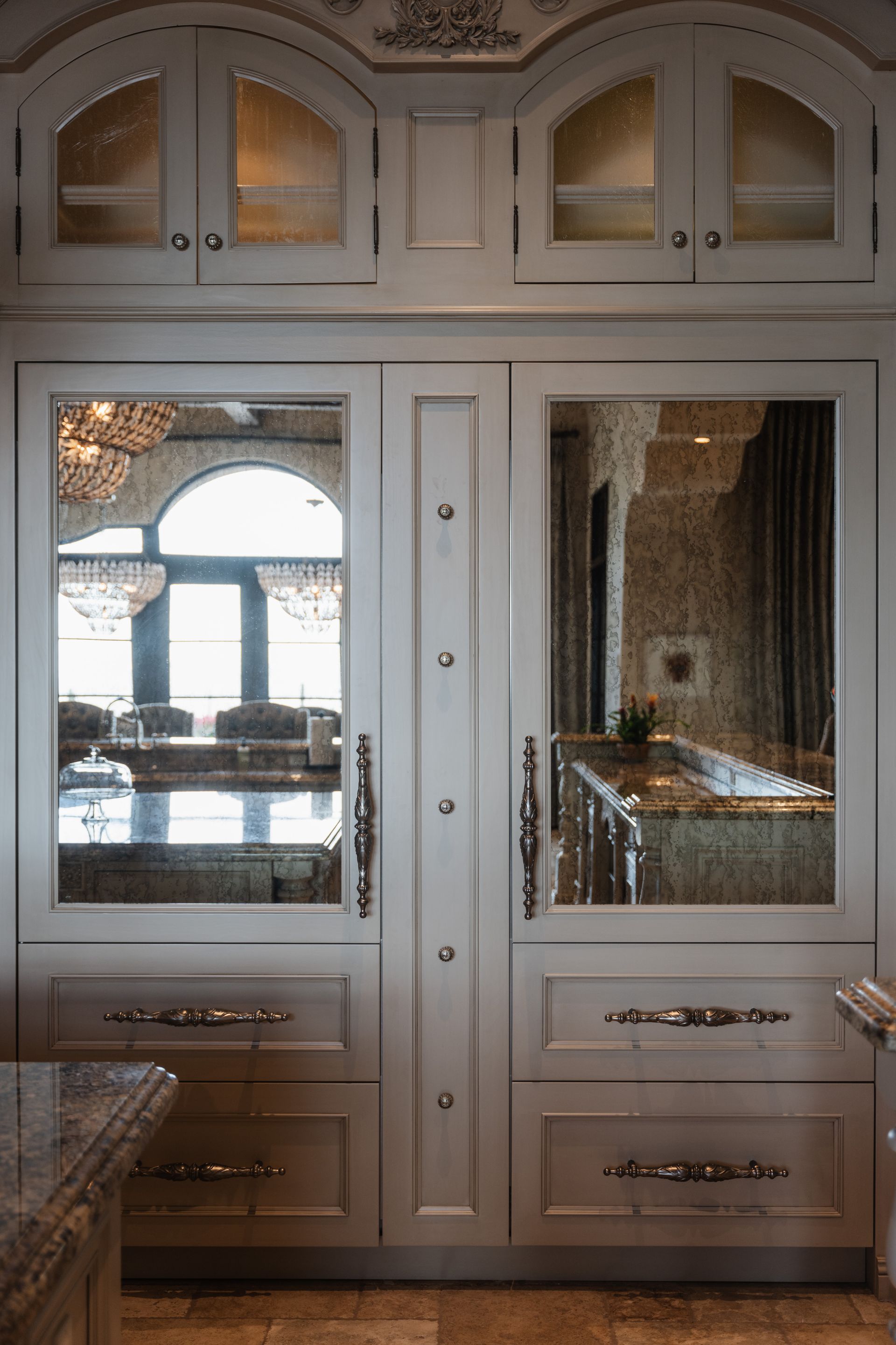 White kitchen cabinets with mirrored doors, reflecting a room with a chandelier and island.