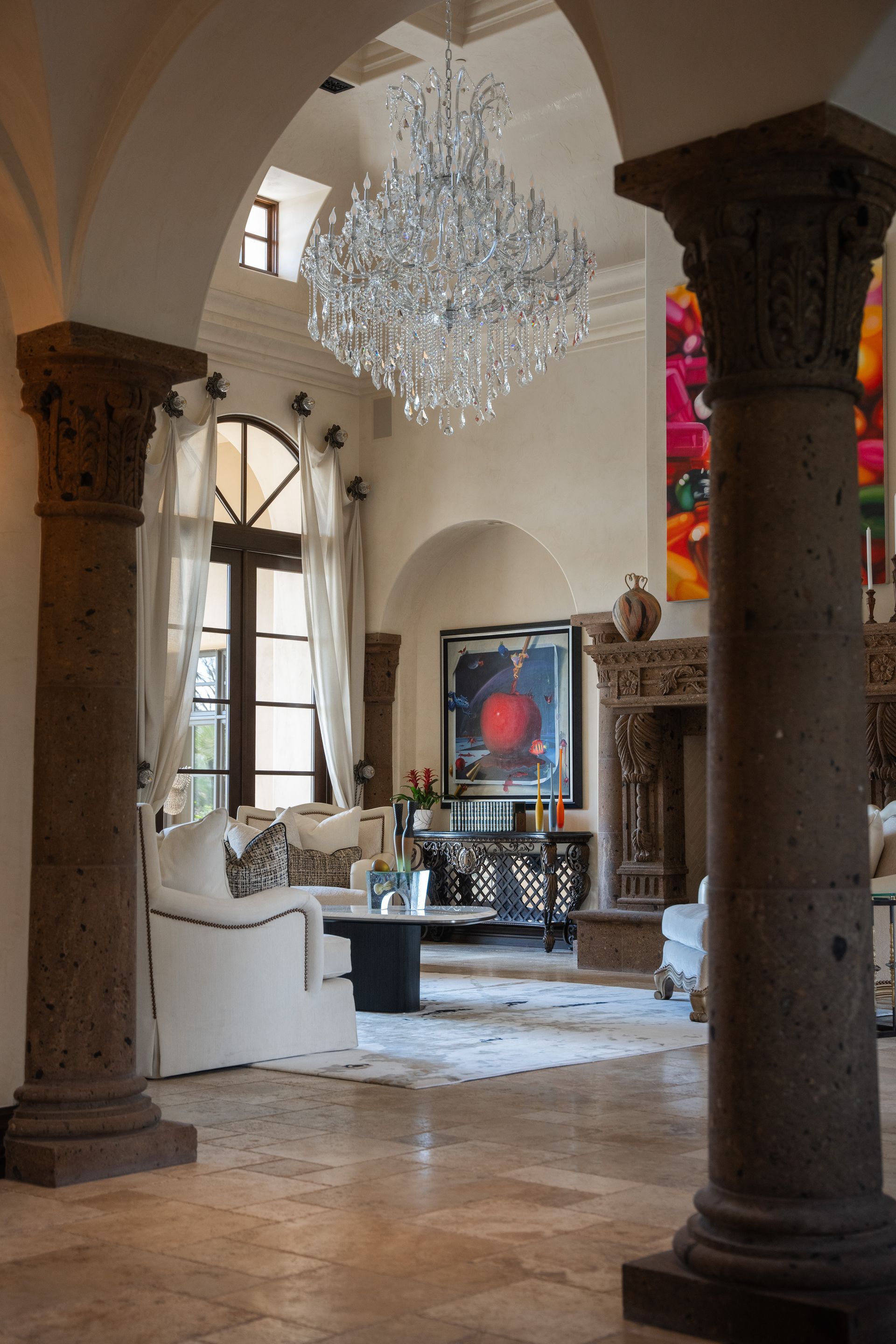 Elegant living room with crystal chandelier, stone columns, white sofa, and colorful artwork.