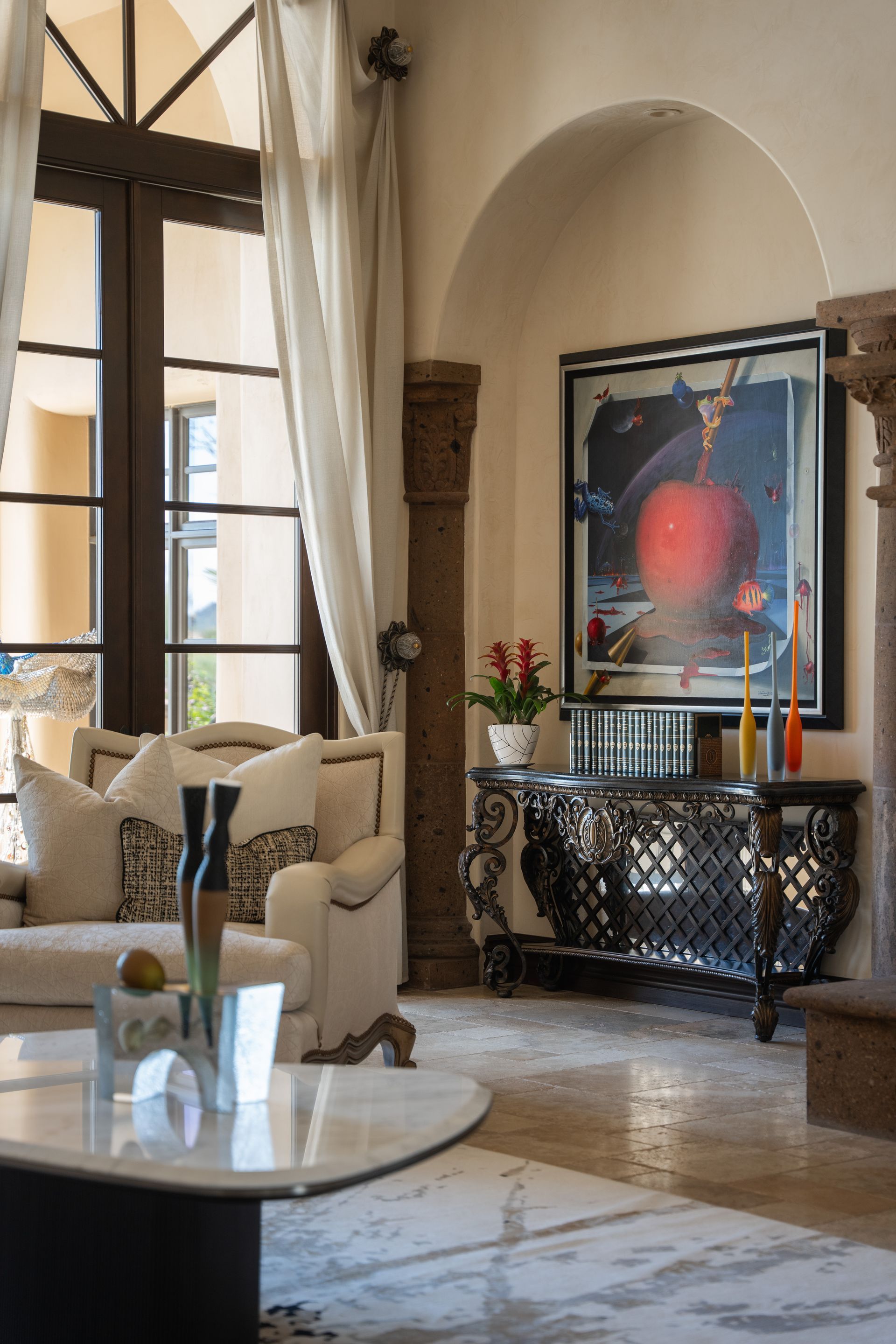 Luxurious living room: cream sofa, ornate console table, large apple artwork, arched doorway, and marble floor.