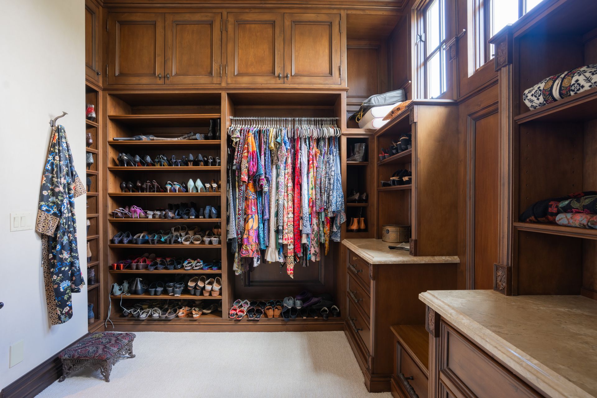 Walk-in closet with dark wood shelving, shoe racks, hanging clothes, and a window.