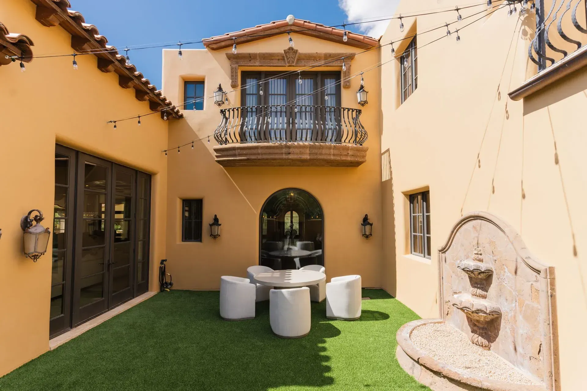 Courtyard with stucco walls, balcony, fountain, and seating area on green turf.