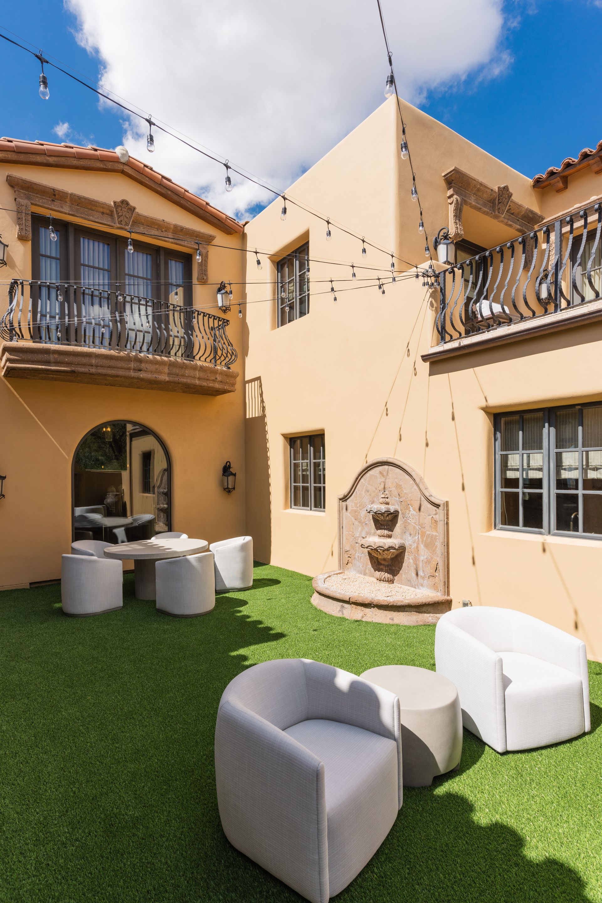 Courtyard with beige stucco buildings, faux grass, seating, string lights, and a fountain.