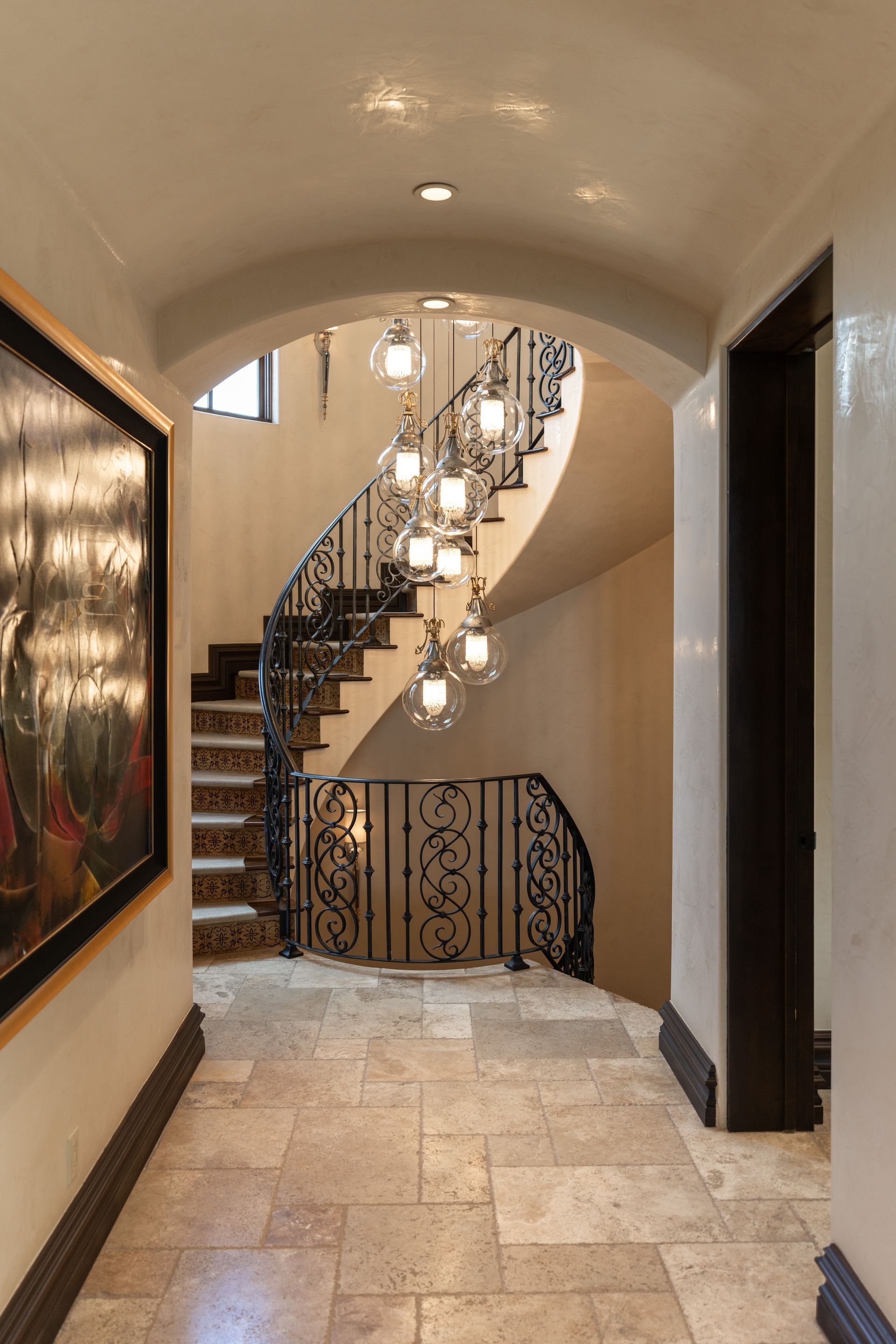 Hallway with curved staircase, wrought iron railing, and a multi-light chandelier.