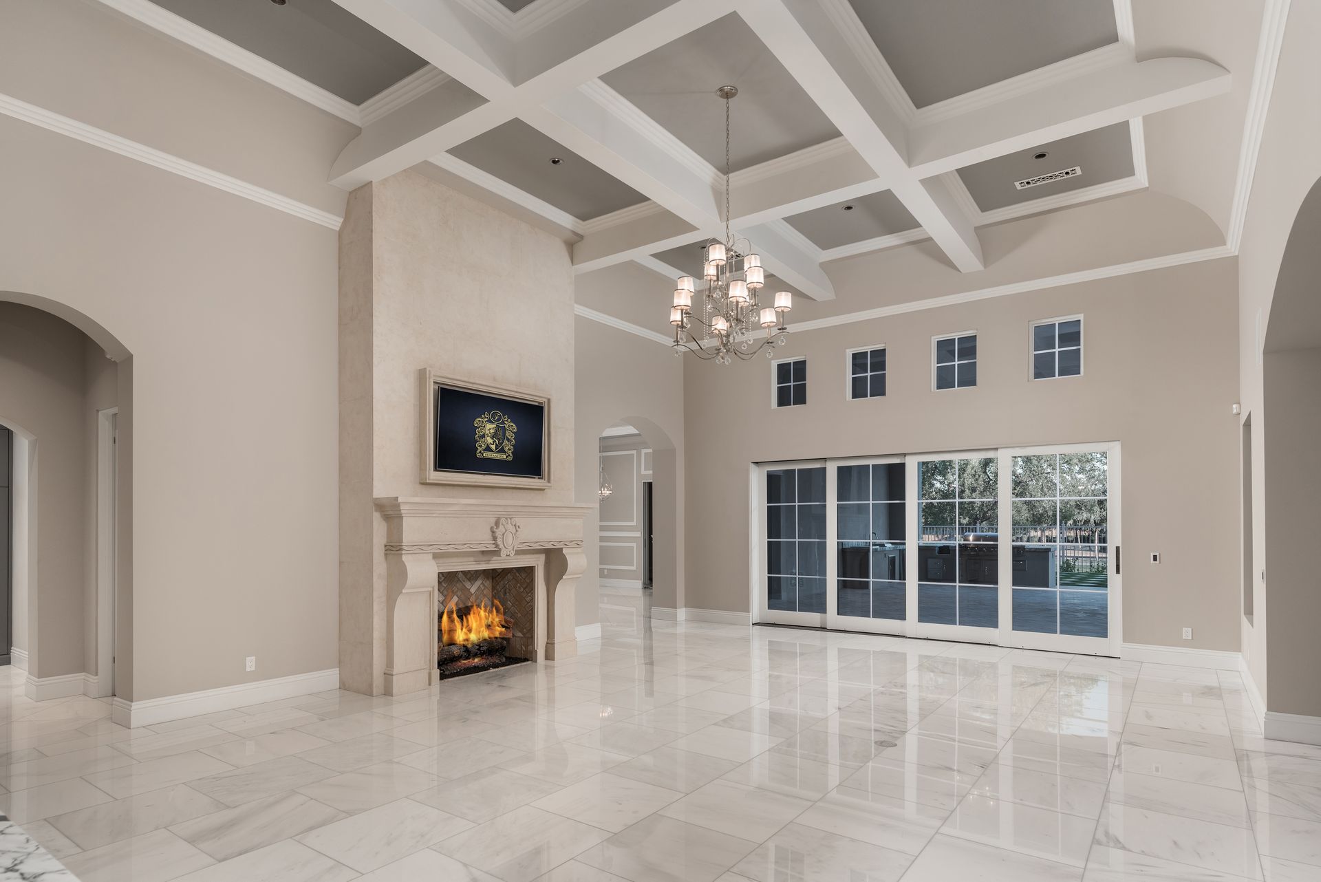 Spacious room with fireplace, chandelier, and sliding glass doors. Light-colored walls and marble floor.