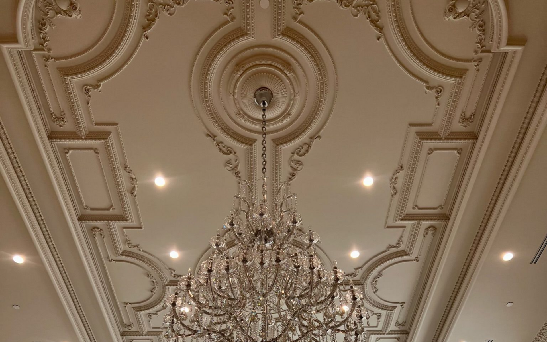 Ornate ceiling with chandelier, gold and white detailing, recessed lights.
