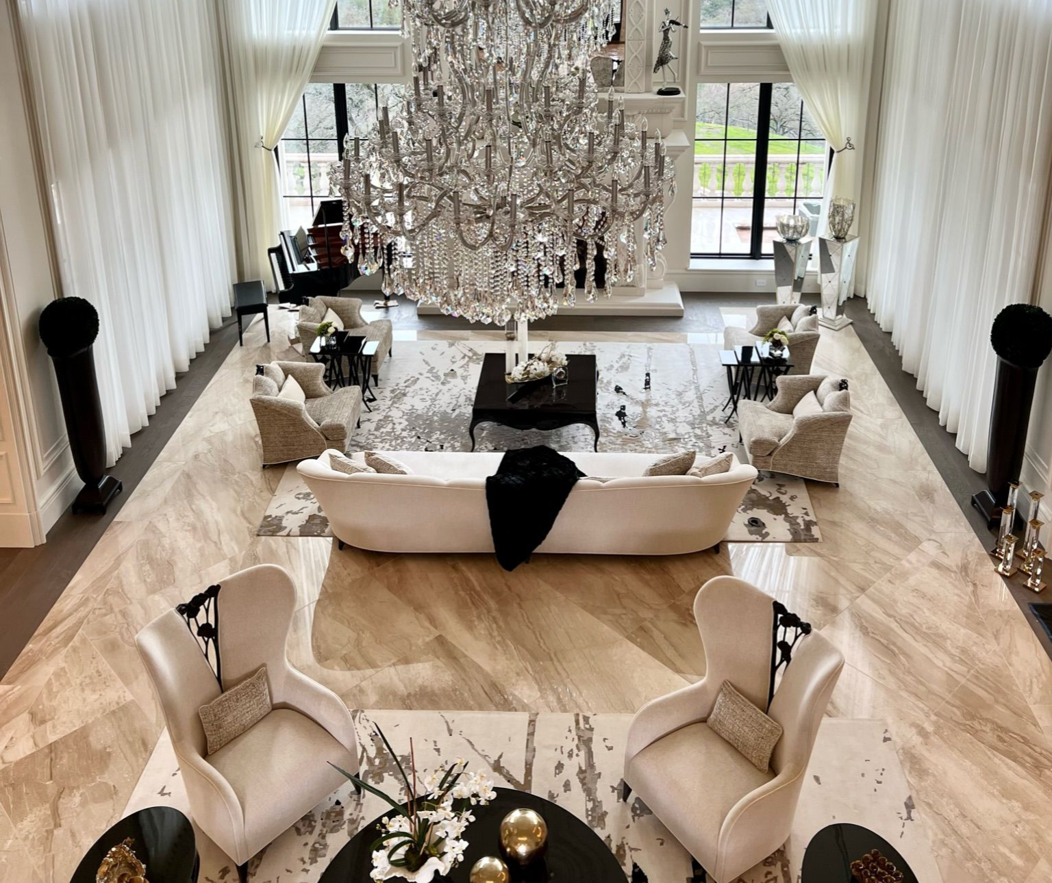 High-angle view of a luxurious living room with chandeliers, seating areas, and a large patterned rug.