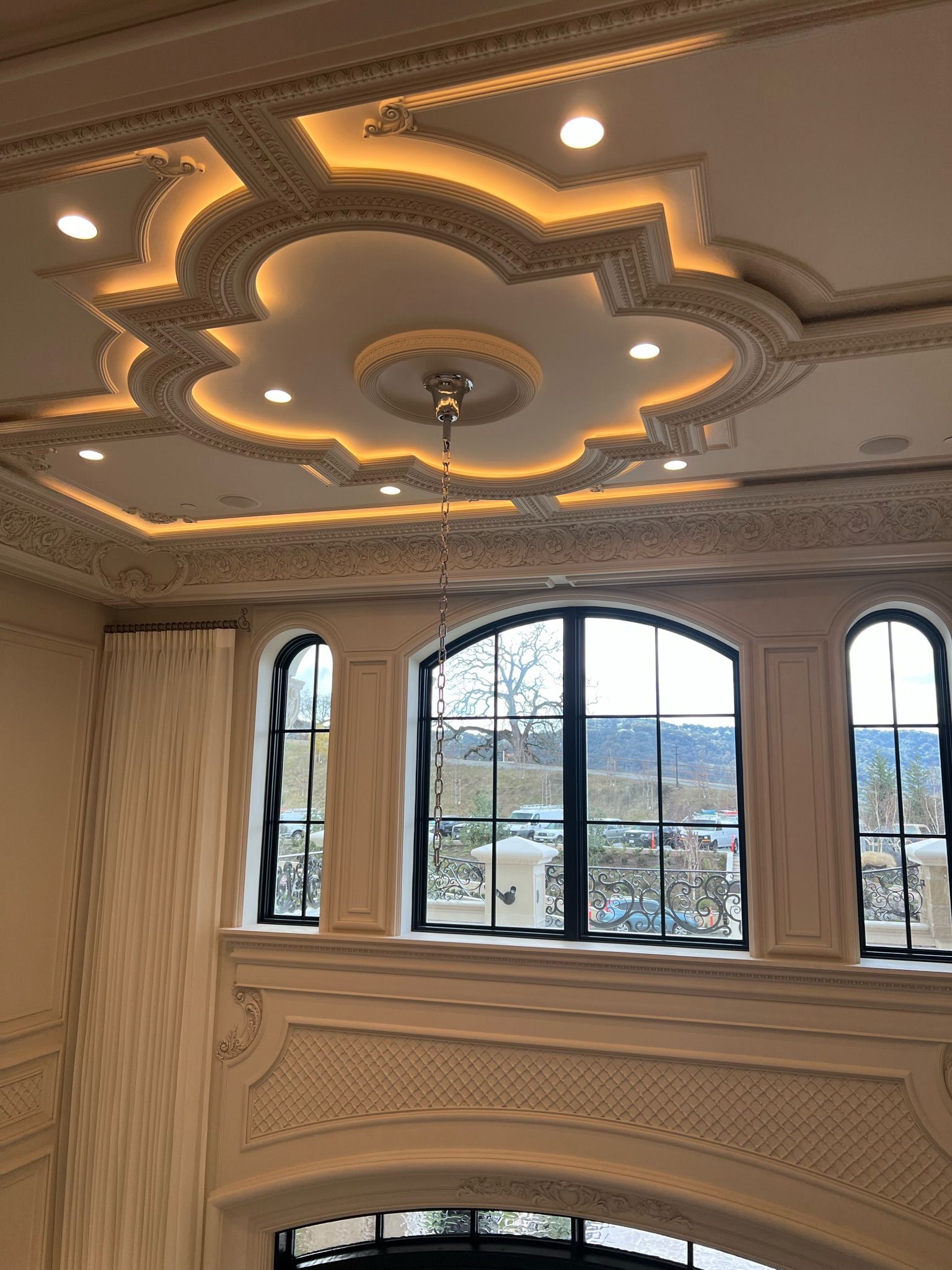 Ornate ceiling with warm lights and arched windows overlooking a balcony and trees