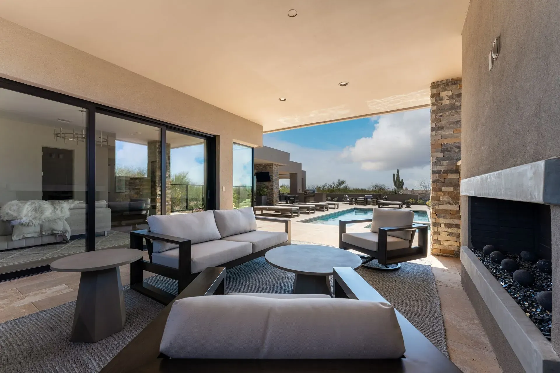 Outdoor living space with sofa, chairs, fireplace, pool, and sliding glass doors.