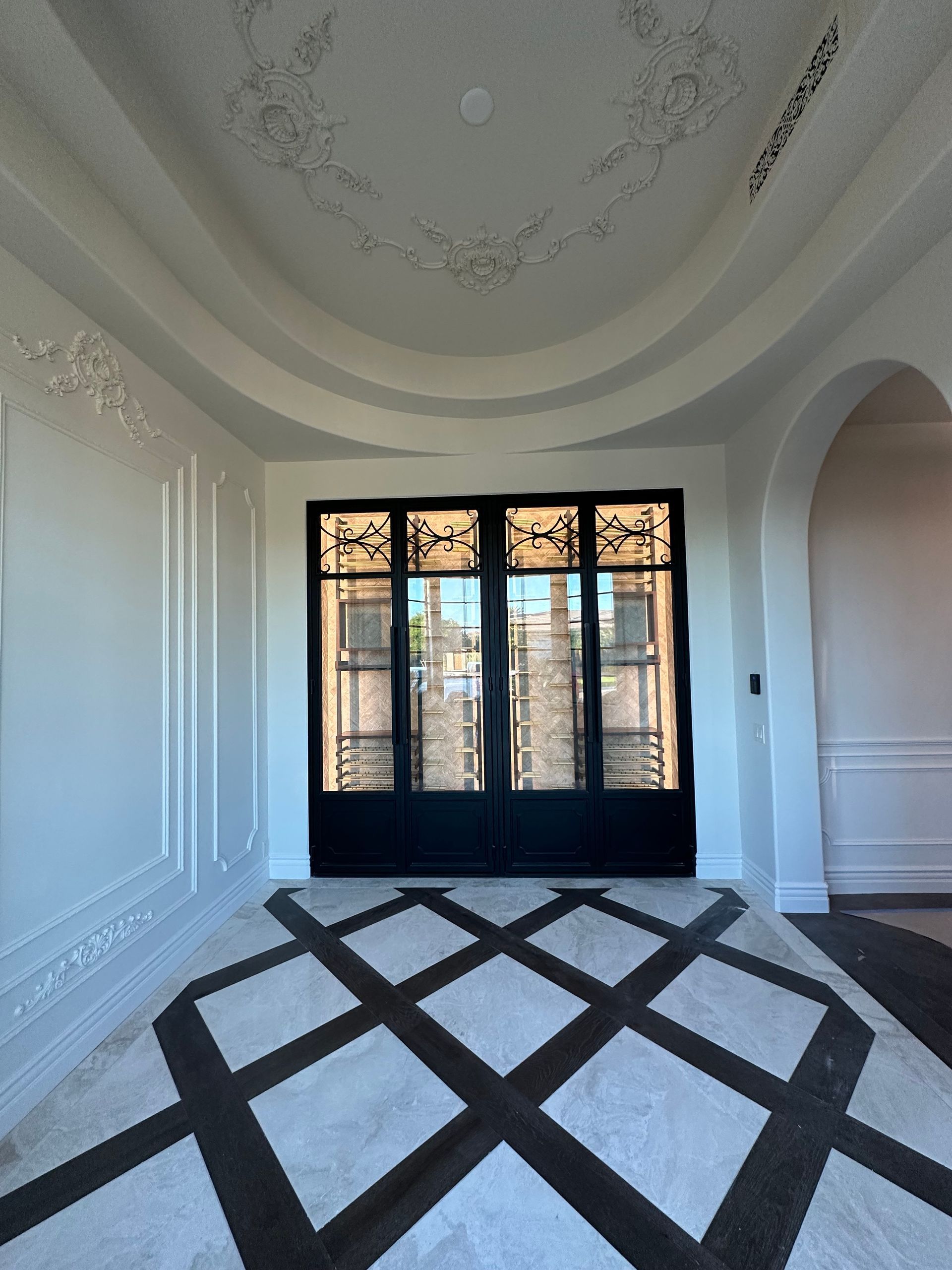 An interior foyer with a coffered ceiling, ornate wall molding, and a black-and-white diamond-patterned stone floor.
