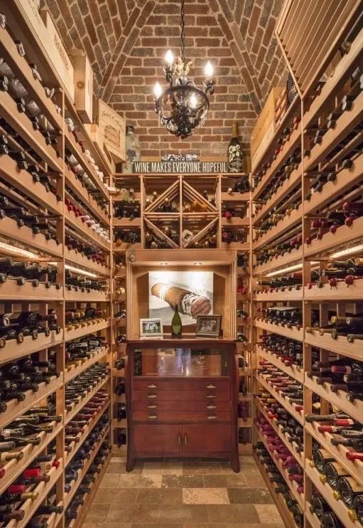Wine cellar with brick arch, wooden racks filled with wine bottles, and a wooden cabinet.