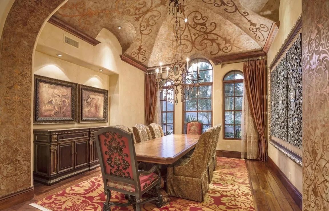 Elegant dining room with ornately painted ceiling, long table, and chandelier.
