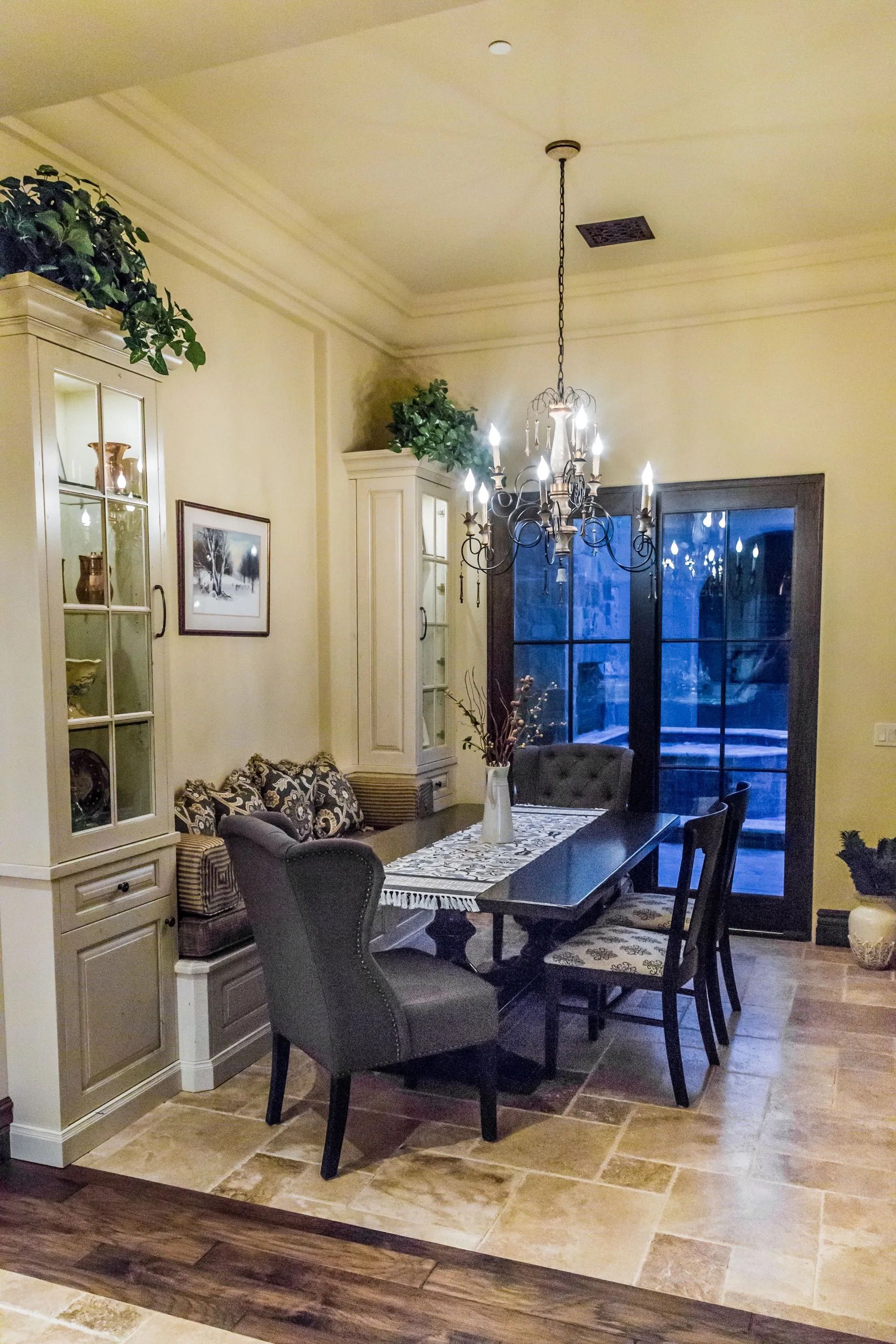 Dining room with long table, chandelier, upholstered chairs, cabinetry, and French doors.