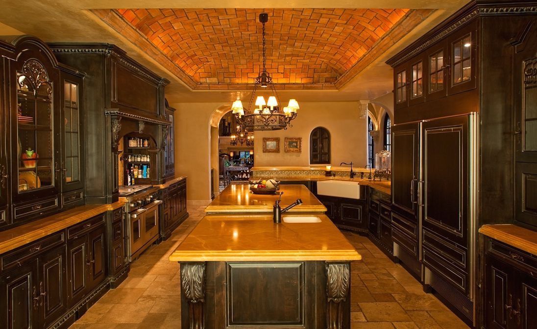 Dark wood kitchen with a stone-like ceiling, long island, and ornate cabinets.